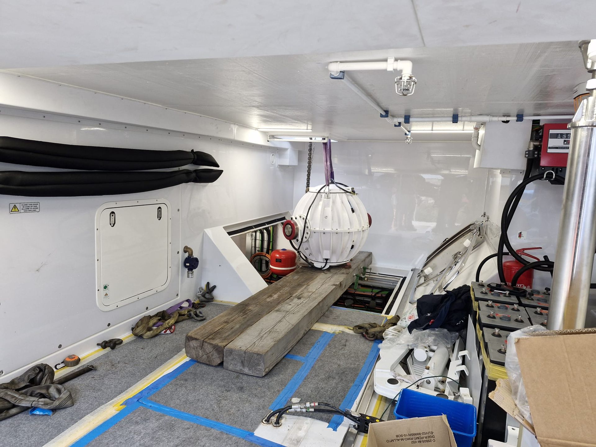 Interno di una stanza bianca con attrezzature, una grande trave di legno e una sfera bianca sospesa.