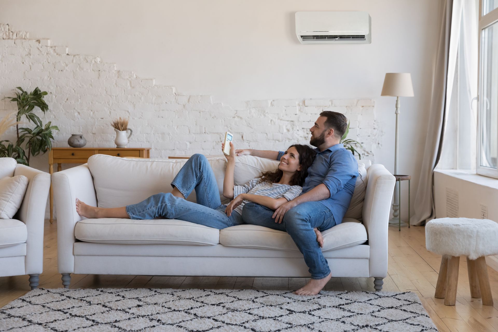 Couple relaxing on a white sofa in a living room, looking at a phone. Air conditioner above them.