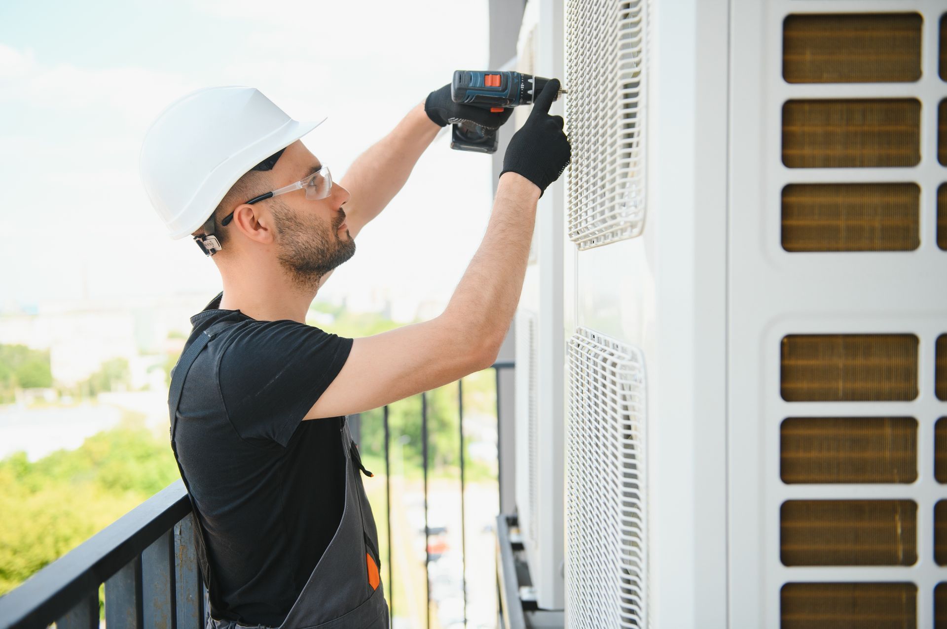 HVAC technician in a hard hat using a drill on an outdoor air conditioning unit.