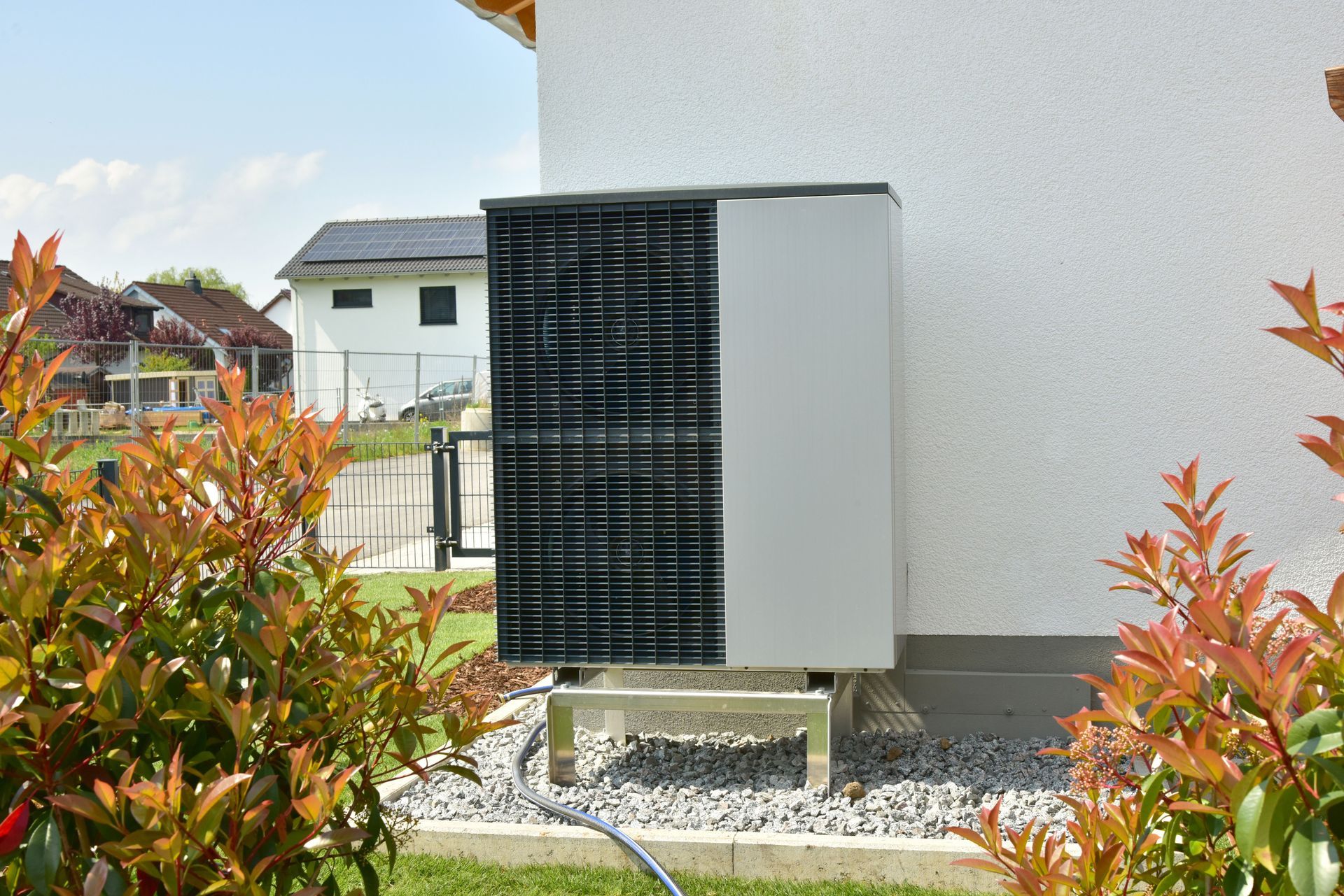 Two air conditioning units sit next to a house with beige siding and a window.