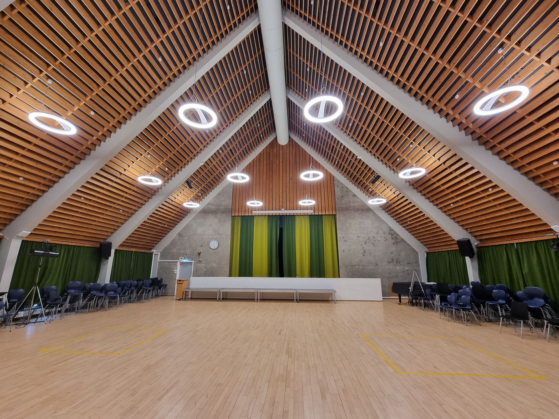 Auditorium med tretak, scene, stoler og sirkulære lys.