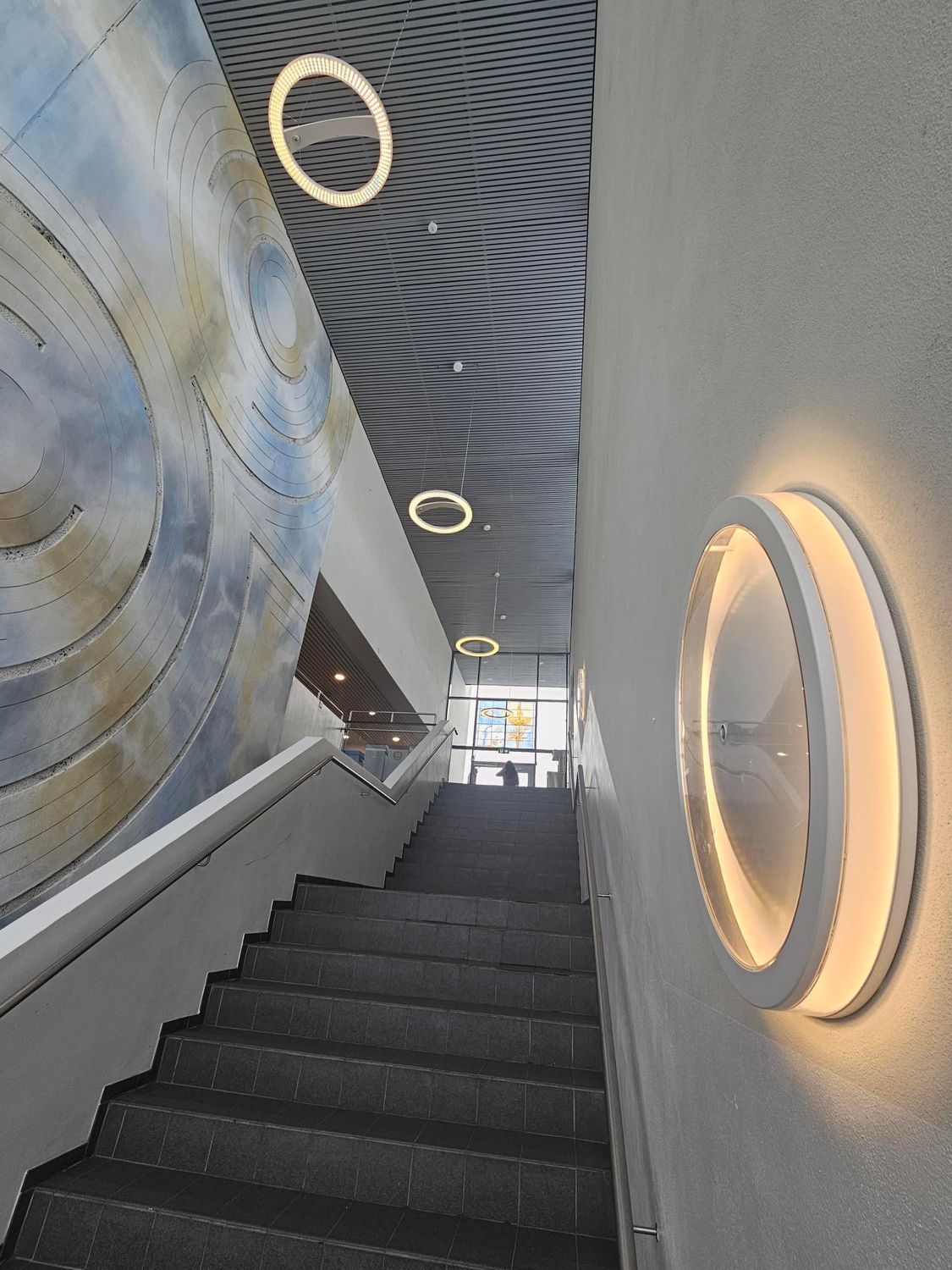 Trappehus med betongtrinn, kunstvegg og sirkulære lys i tak og på vegg.