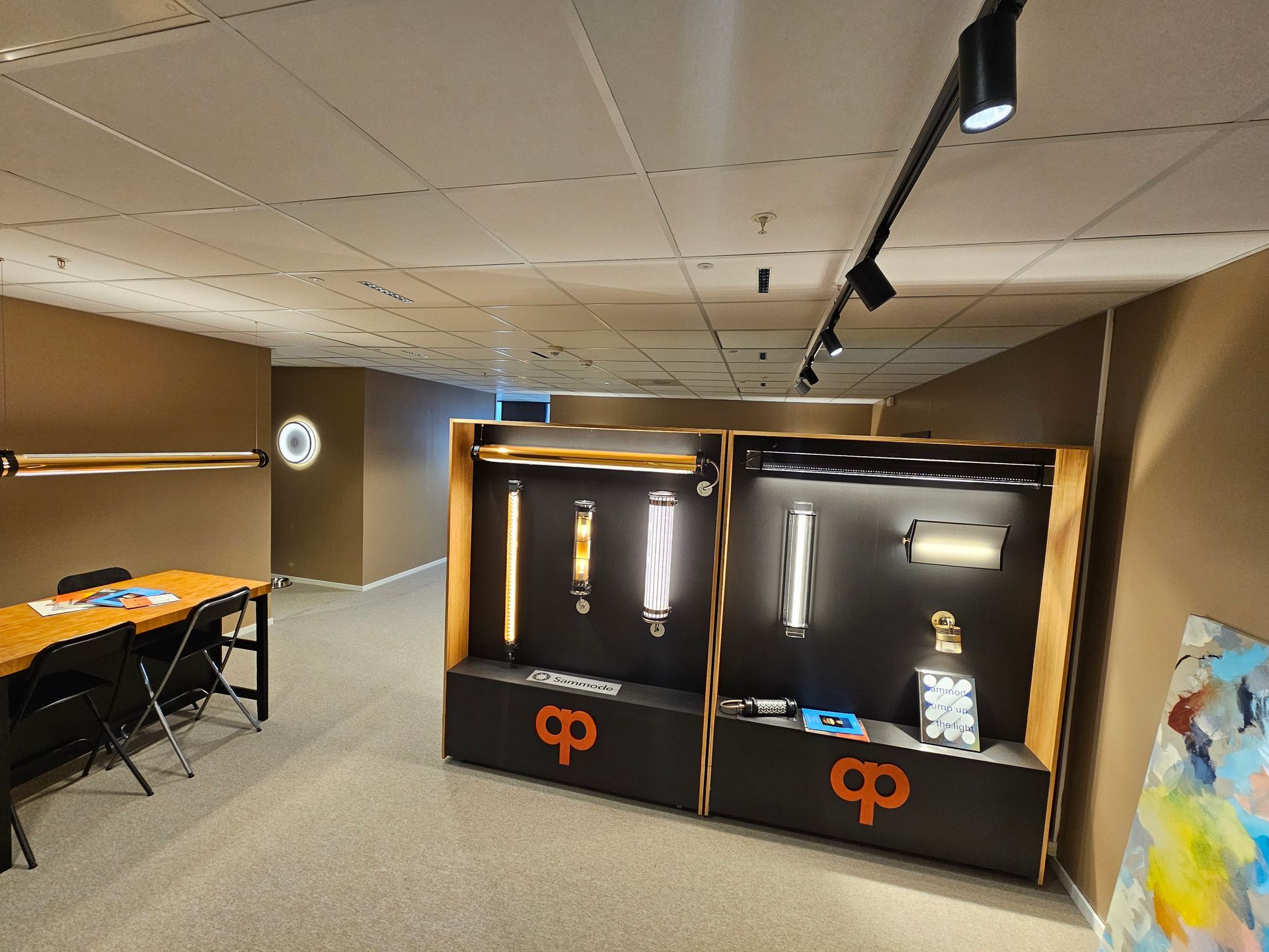 Interiør i et belysningsshowroom med utstillinger av lyspærer, skinnebelysning og et bord. Brune og svarte toner.