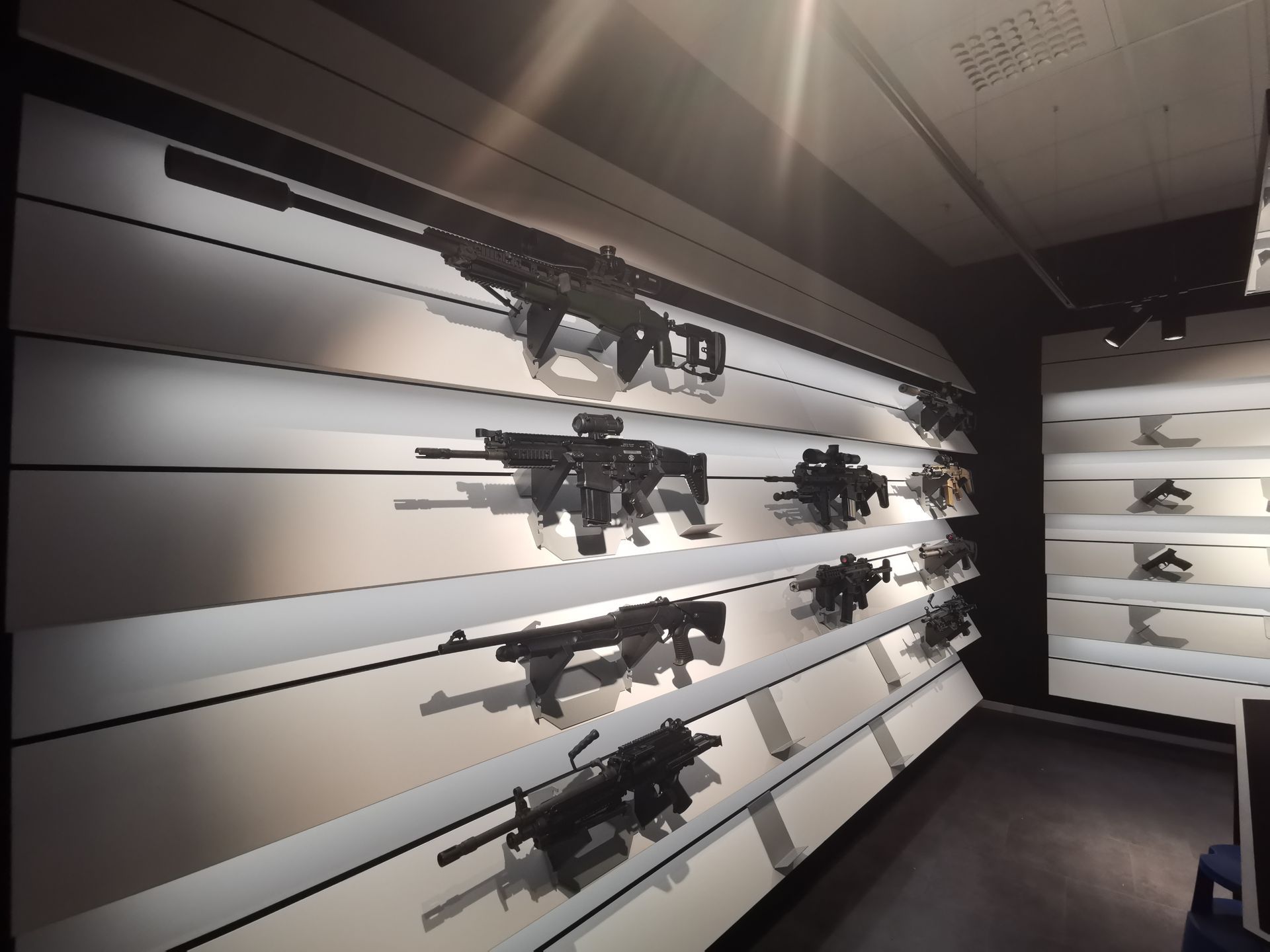 Våpen utstilt på vinklede hvite hyller i et mørkt rom.