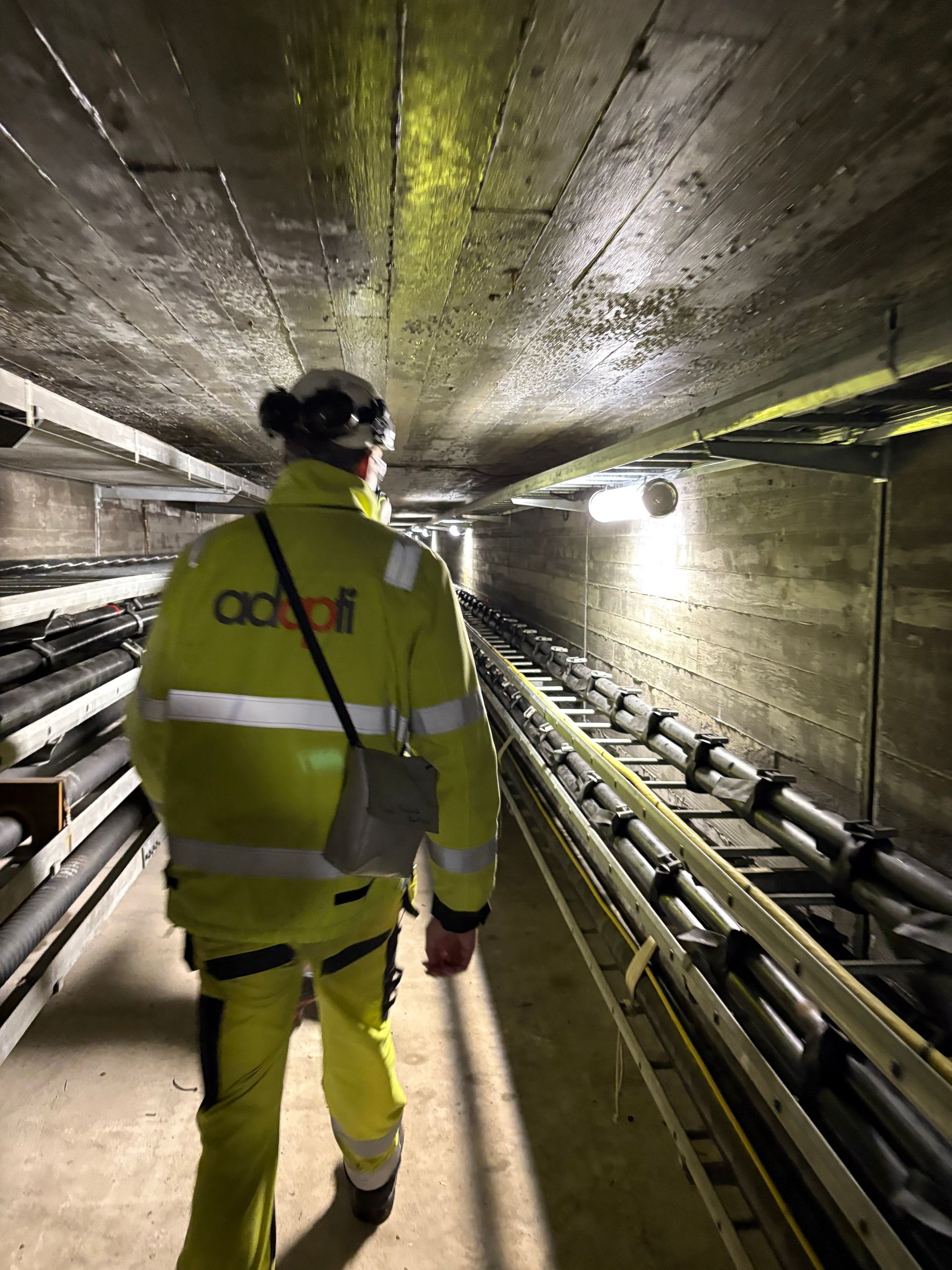 En person i gult sikkerhetsutstyr går gjennom en underjordisk kabeltunnel.