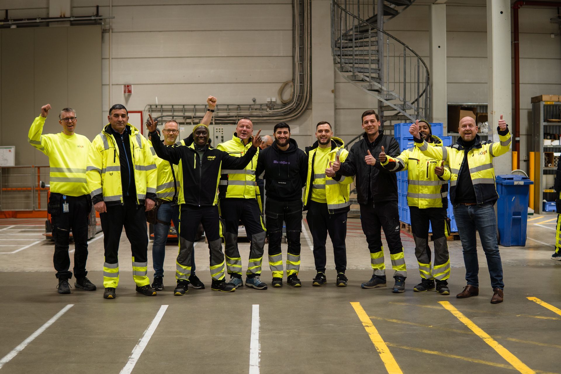 Gruppe mennesker i gule sikkerhetsvester feirer på et lager.