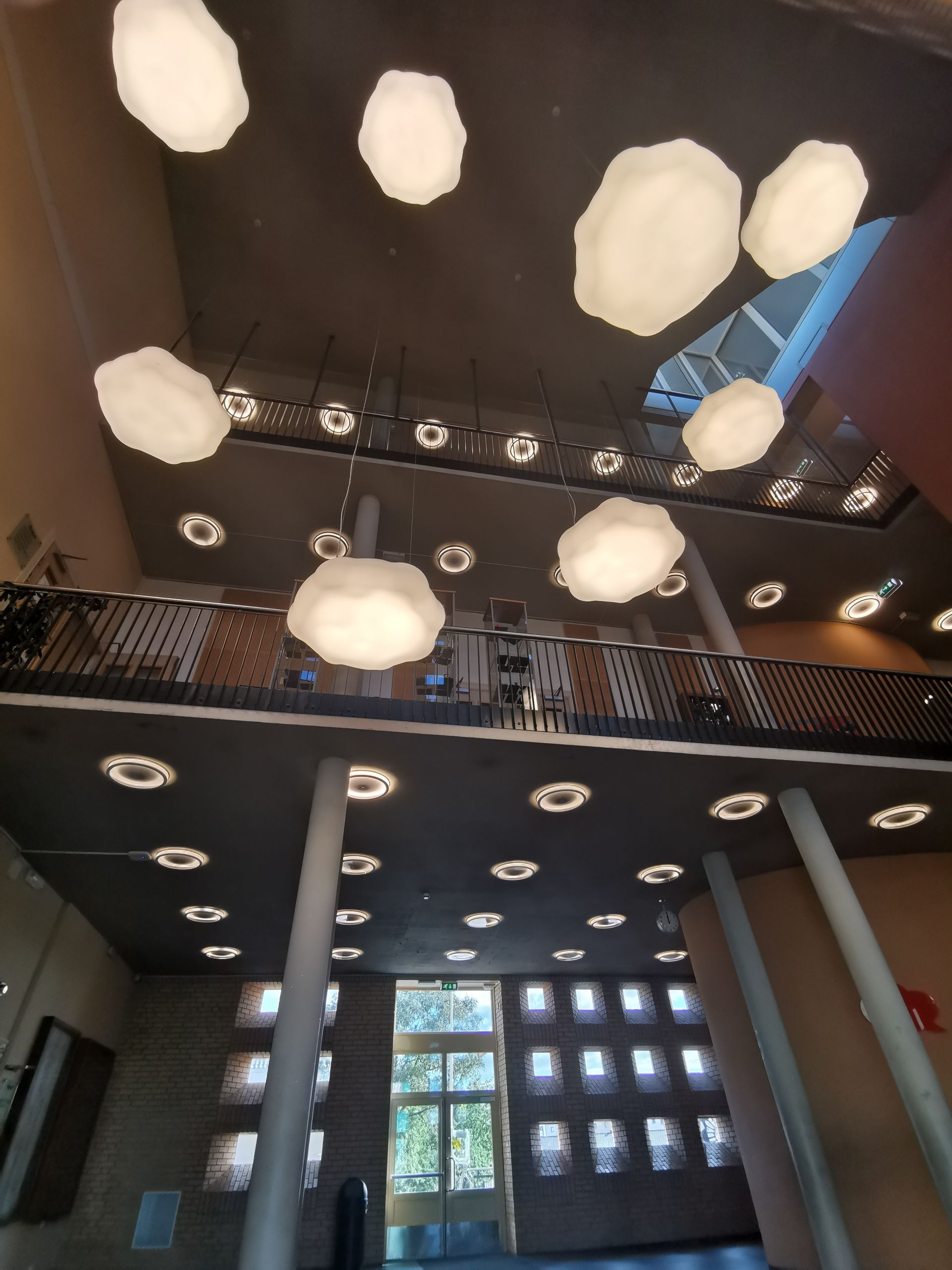 Innvendig utsikt over en bygning med skyformede lys som henger fra taket. En balkong er synlig ovenfor.