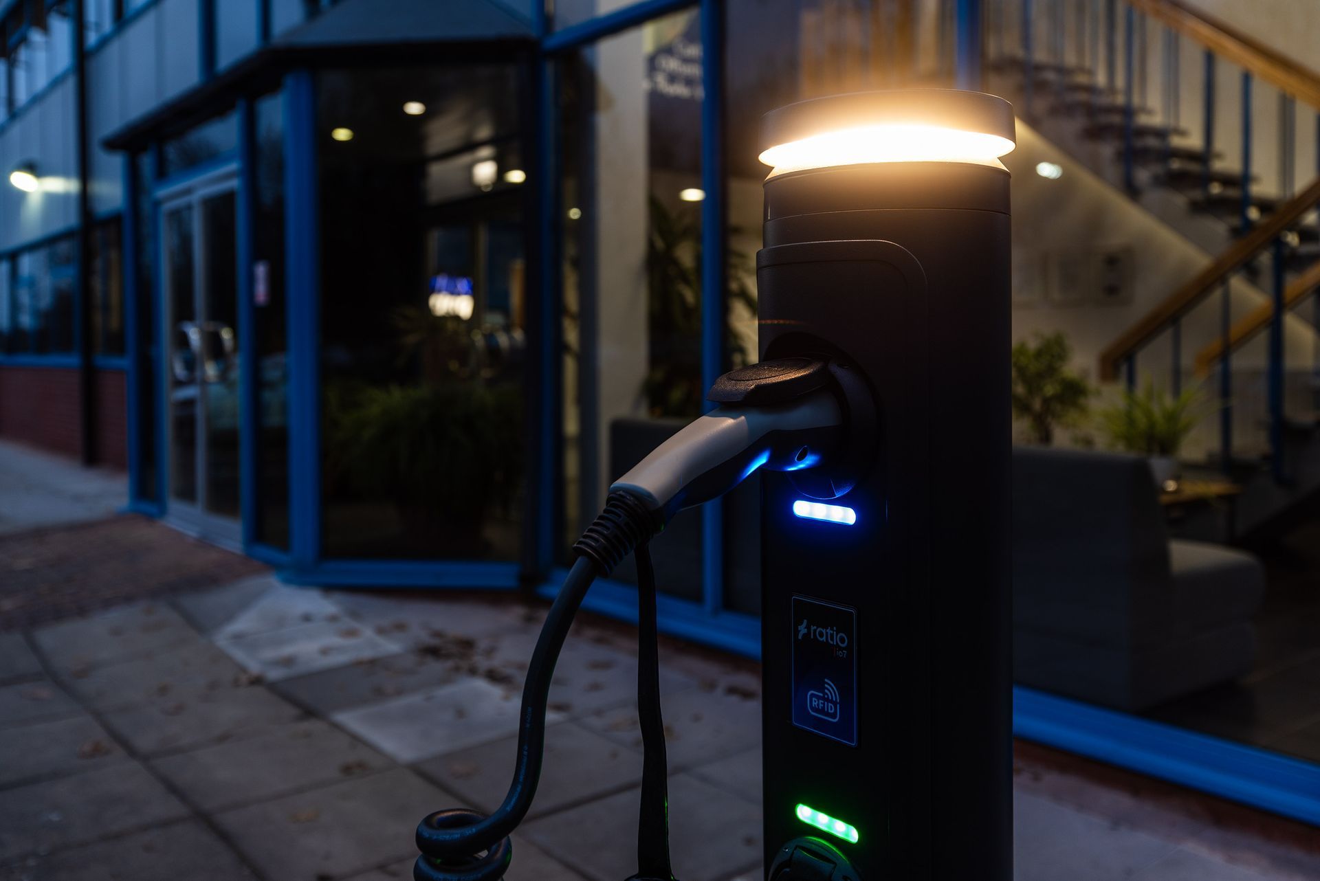 Ladestasjon for elbil utenfor en bygning om natten, opplyst med en lysende topp.