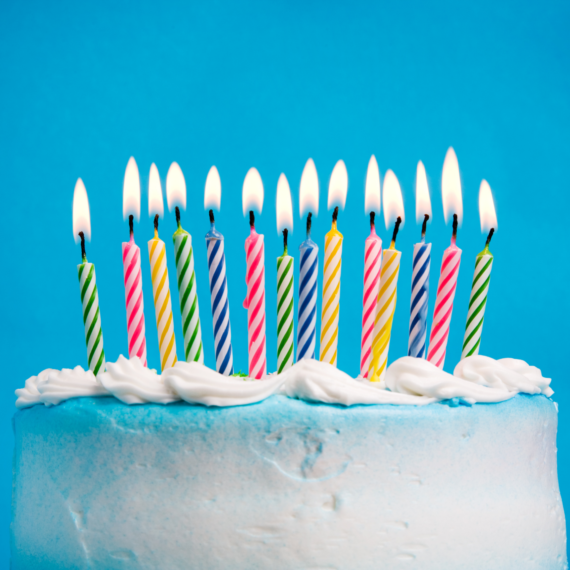 Birthday cake with blue frosting and lit colorful candles.