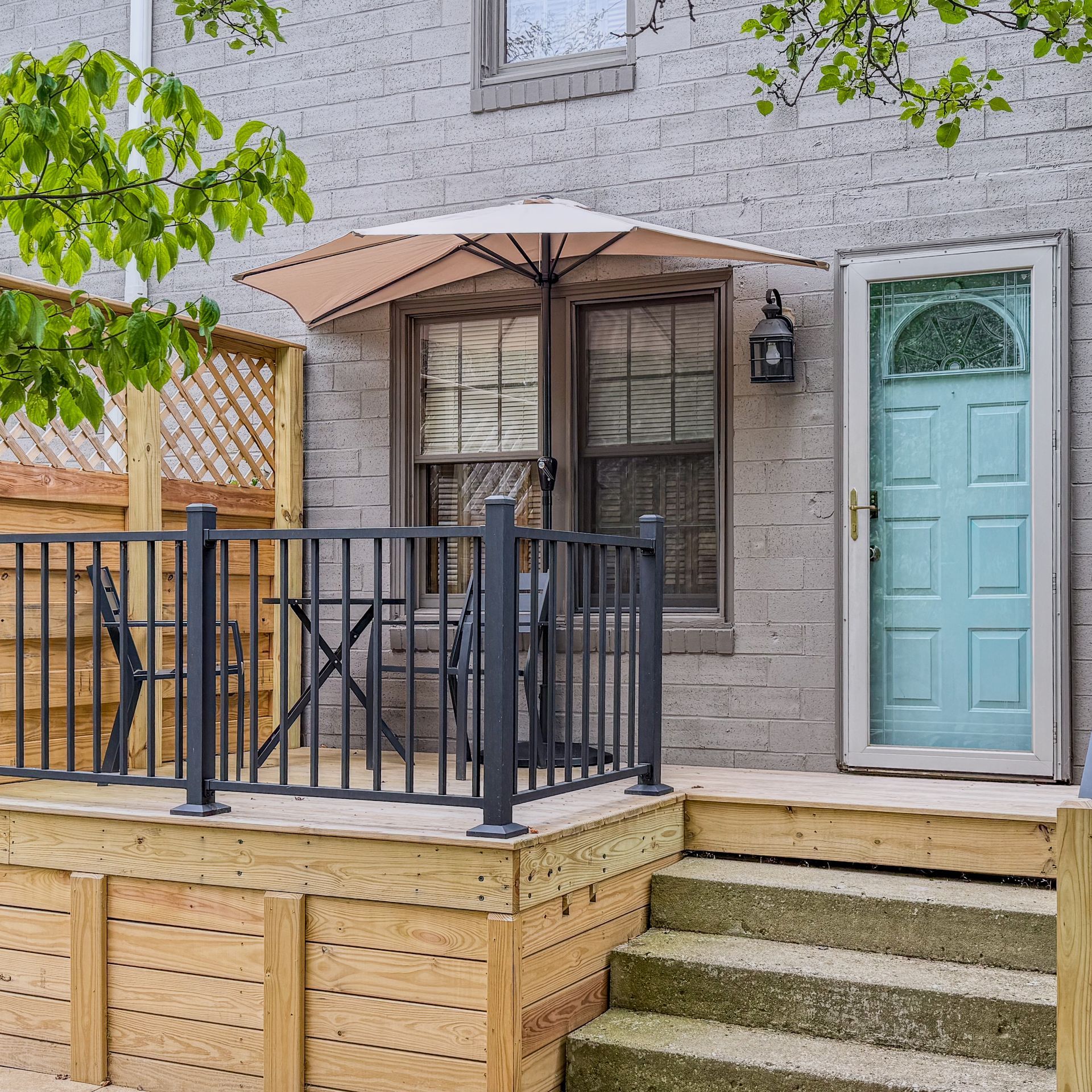 Small patio with a table, chairs, and a blue door. Umbrella shades a window.