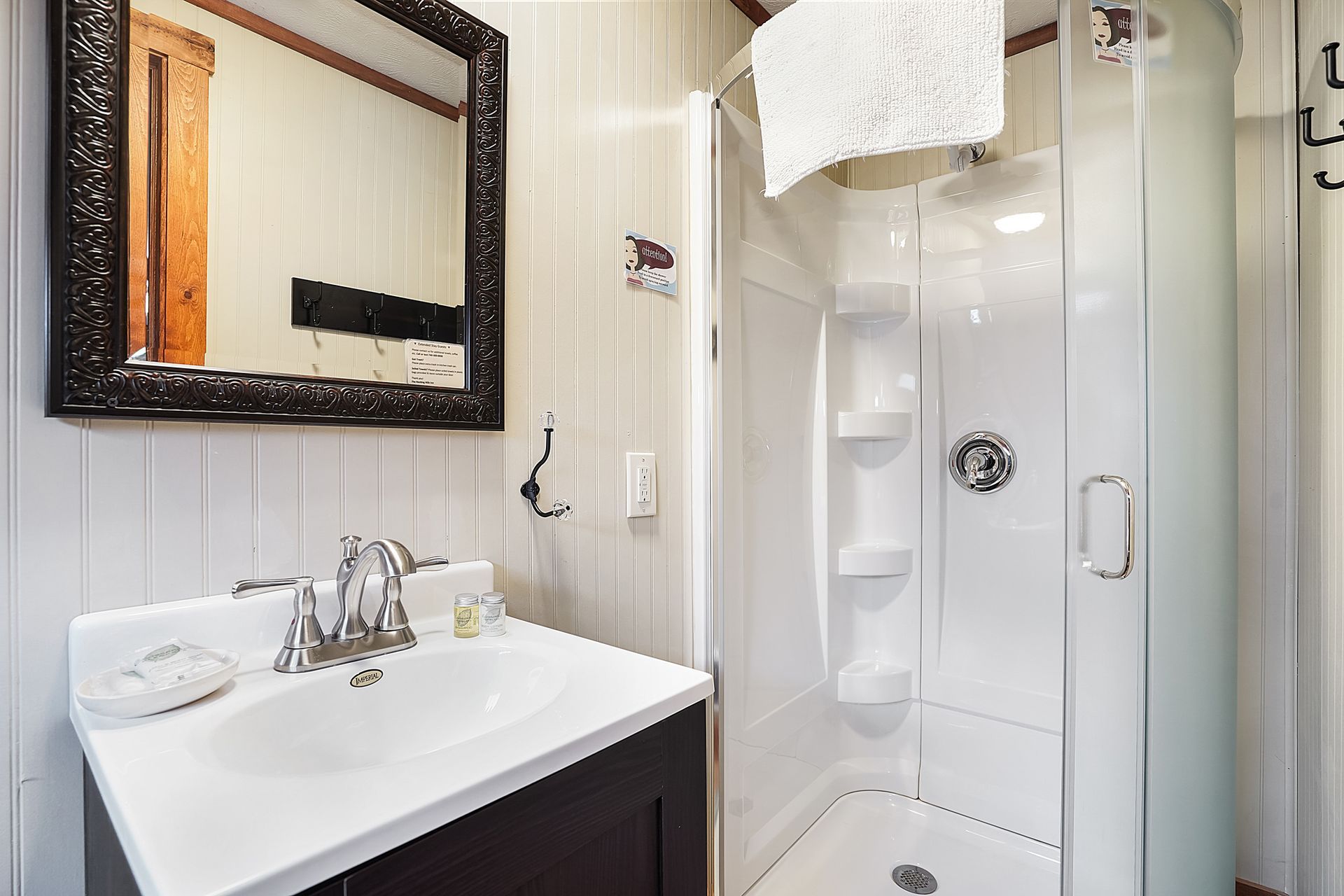 Small bathroom with a white sink, shower stall, and mirror. The walls are white and the mirror has a dark frame.