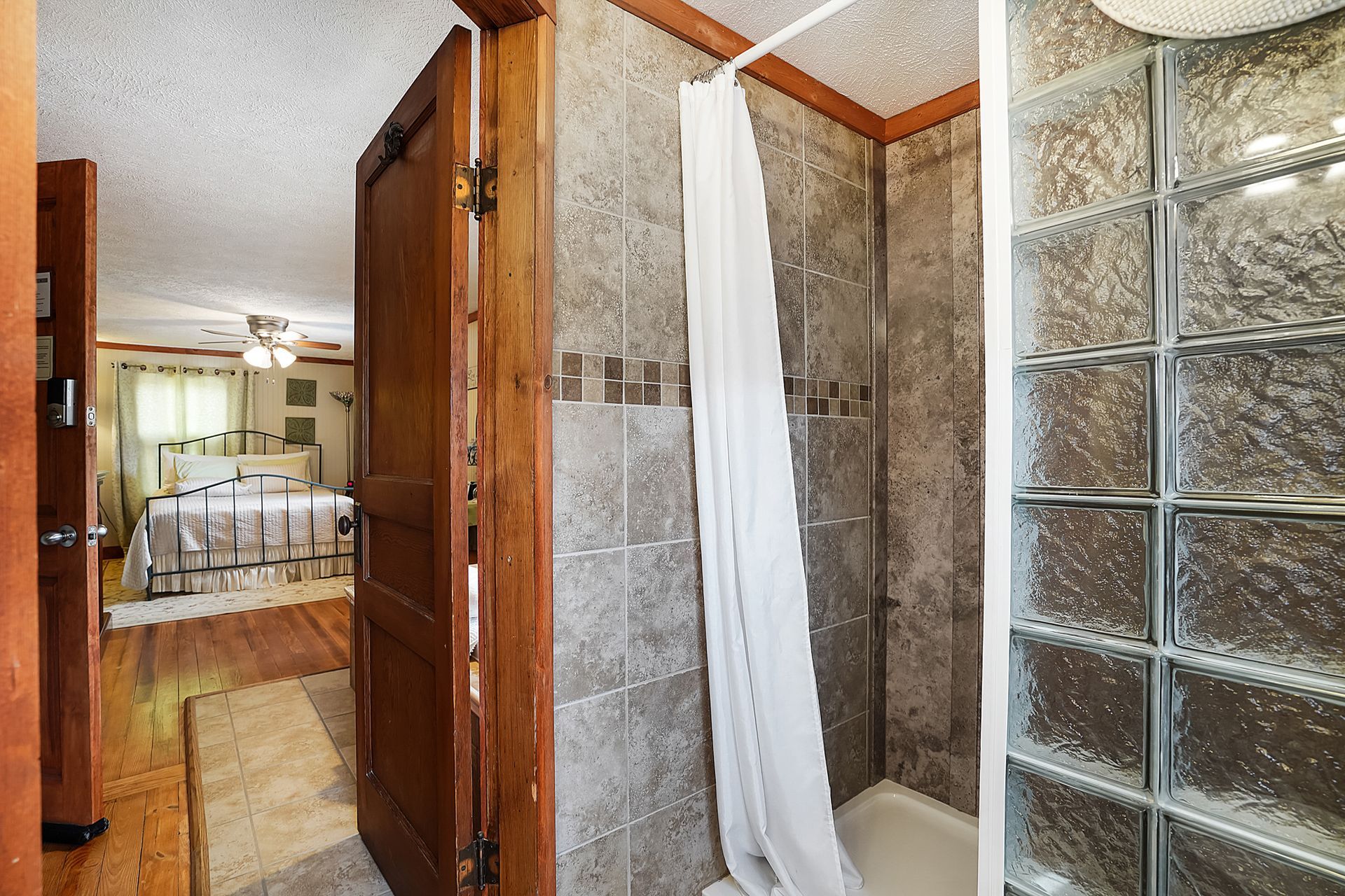 Bathroom with a shower behind a glass block wall and a partially open wooden door leading to a bedroom.