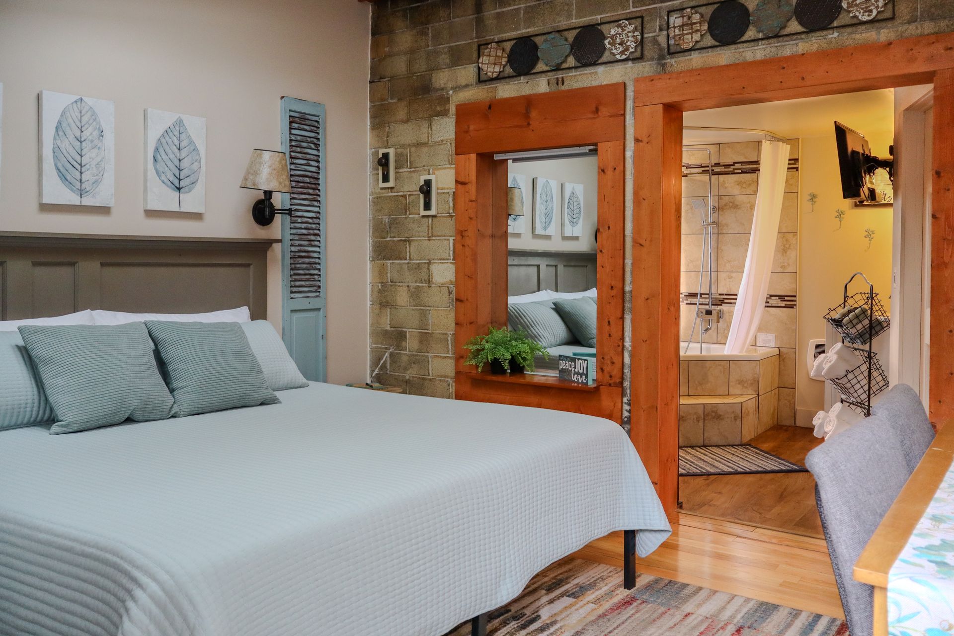 Cozy bedroom with a king-size bed, opening to a bathroom. The room has exposed stone walls and three wall art pieces.