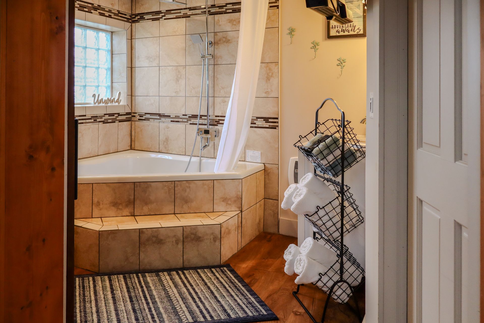 Bathroom interior with a corner bathtub, tiled walls, and a towel rack viewed from a doorway.
