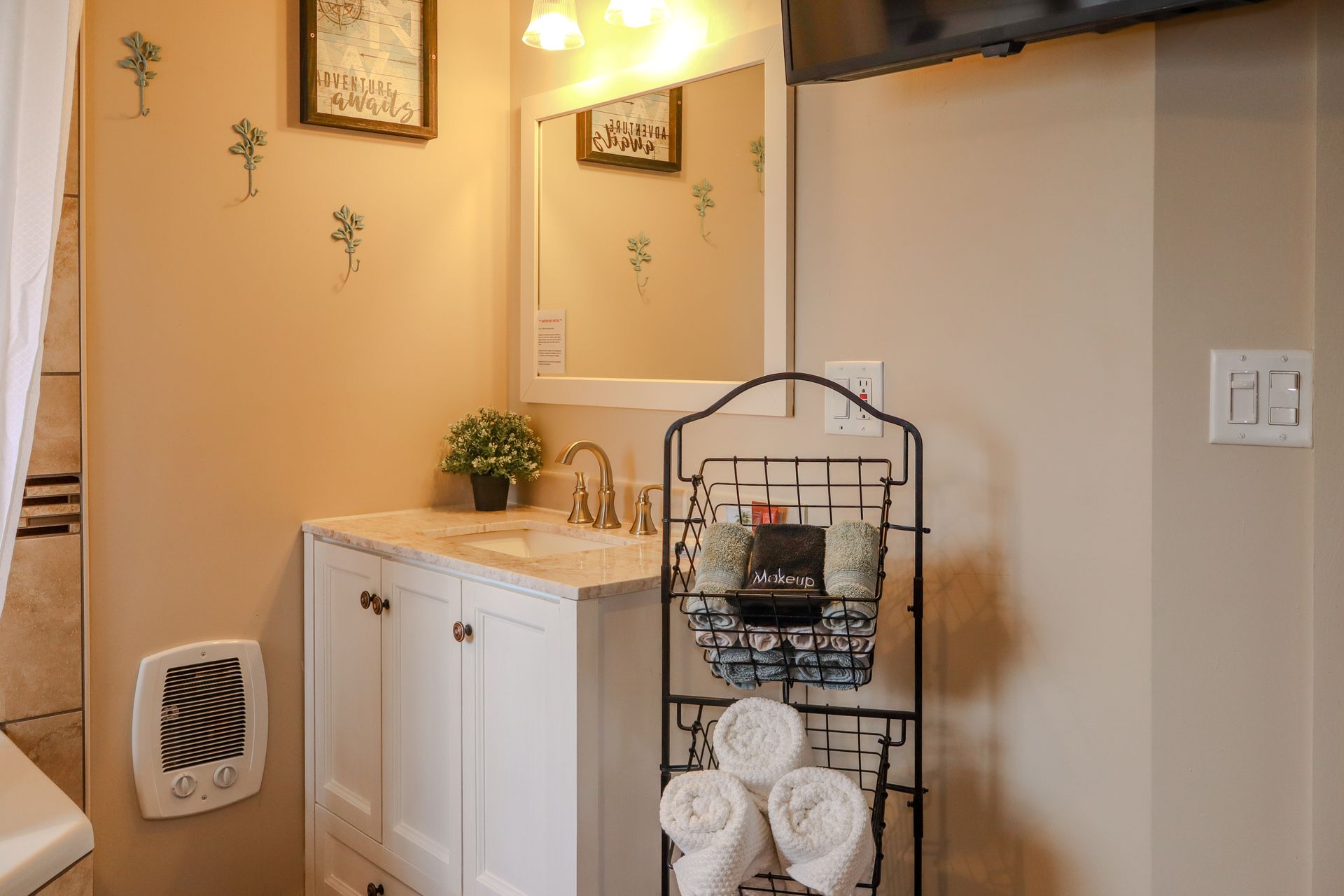 Bathroom with a white vanity, mirror, and shelving unit holding towels and toiletries.