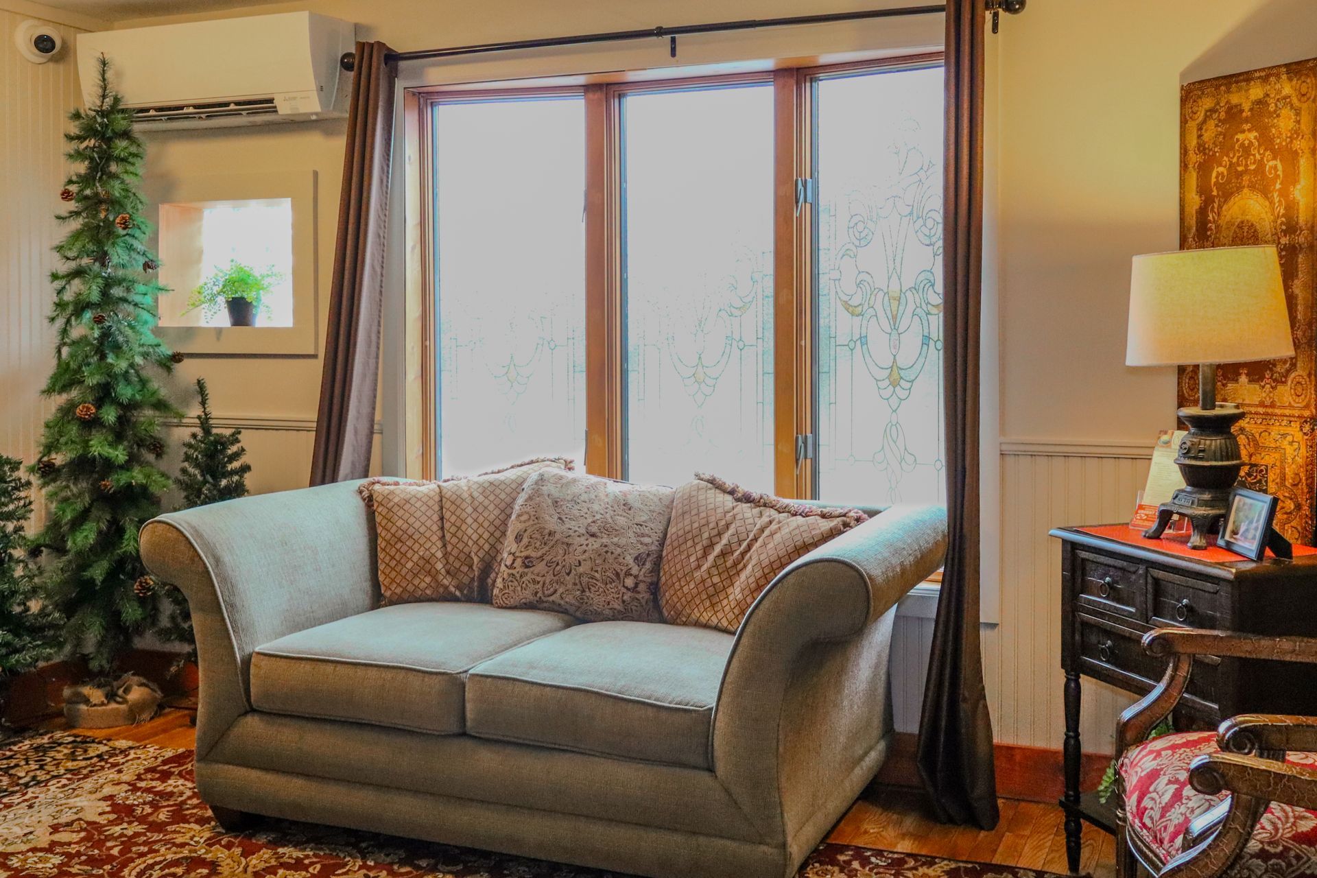 Cozy living room with a loveseat, Christmas tree, and a window. A side table with a lamp sits nearby.