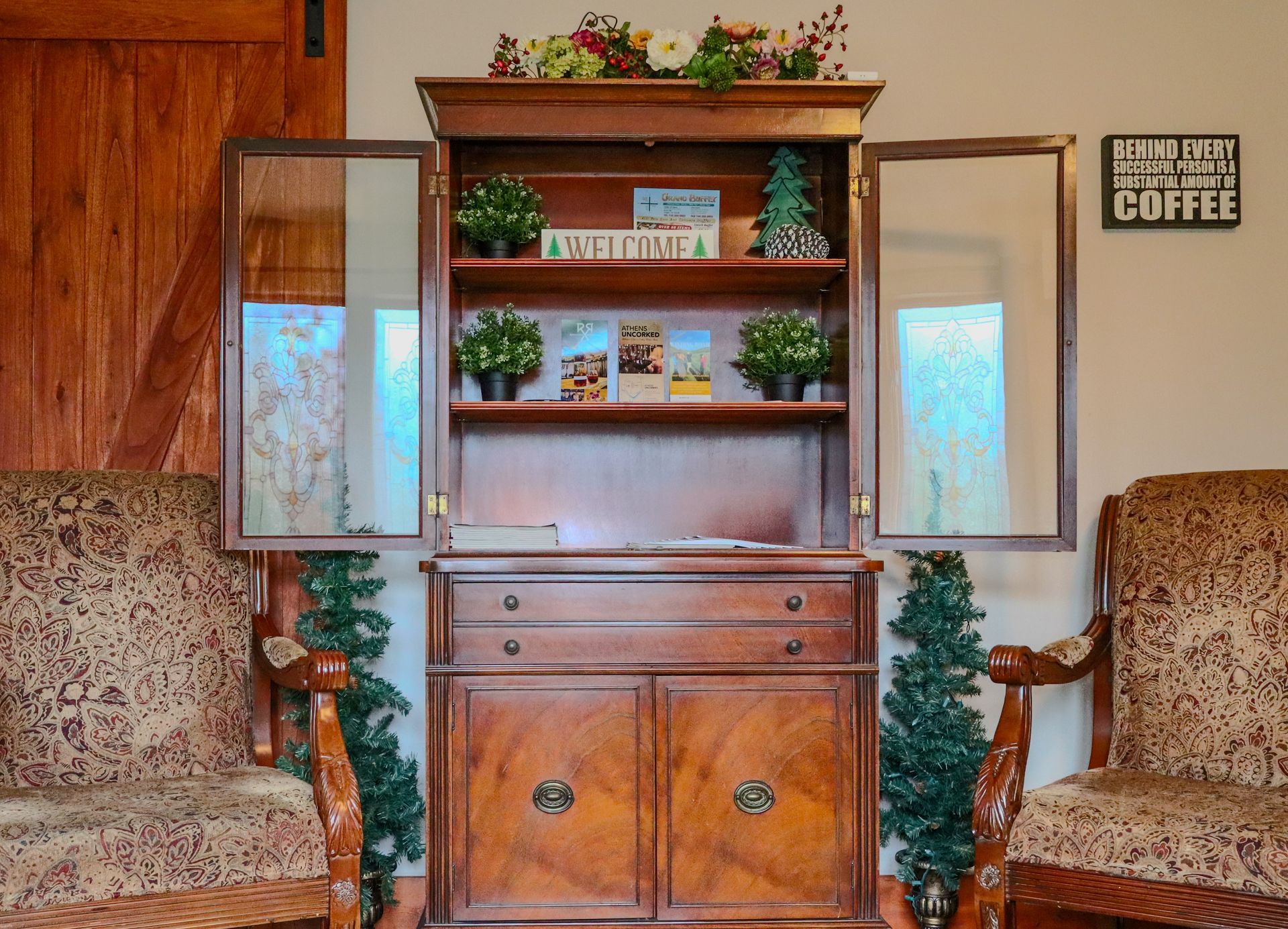 Wooden cabinet with open doors, flanked by chairs, holding plants and postcards.  A