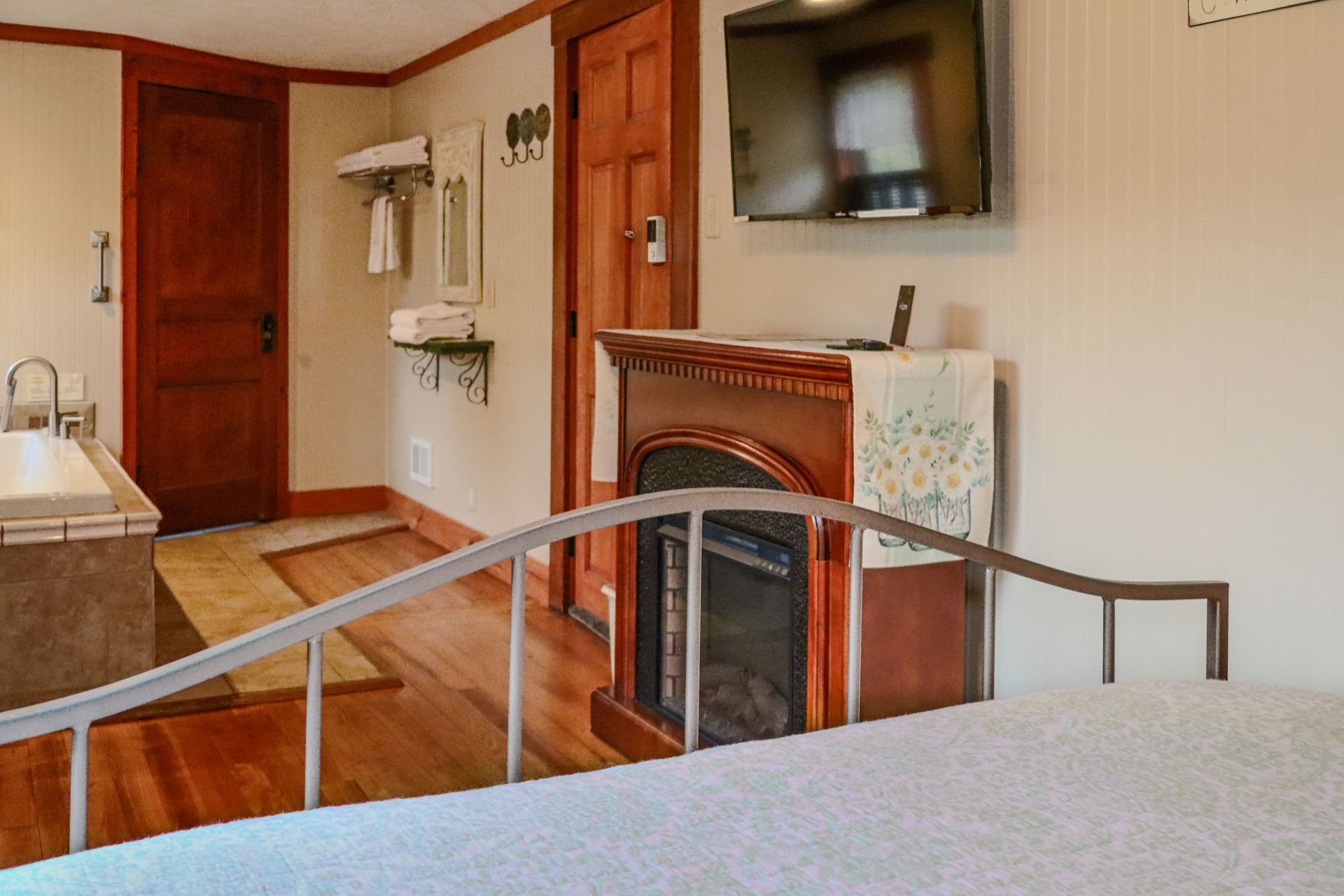 Bedroom with a wooden door, a fireplace, and a television mounted on the wall. There's a bathroom visible in the background.