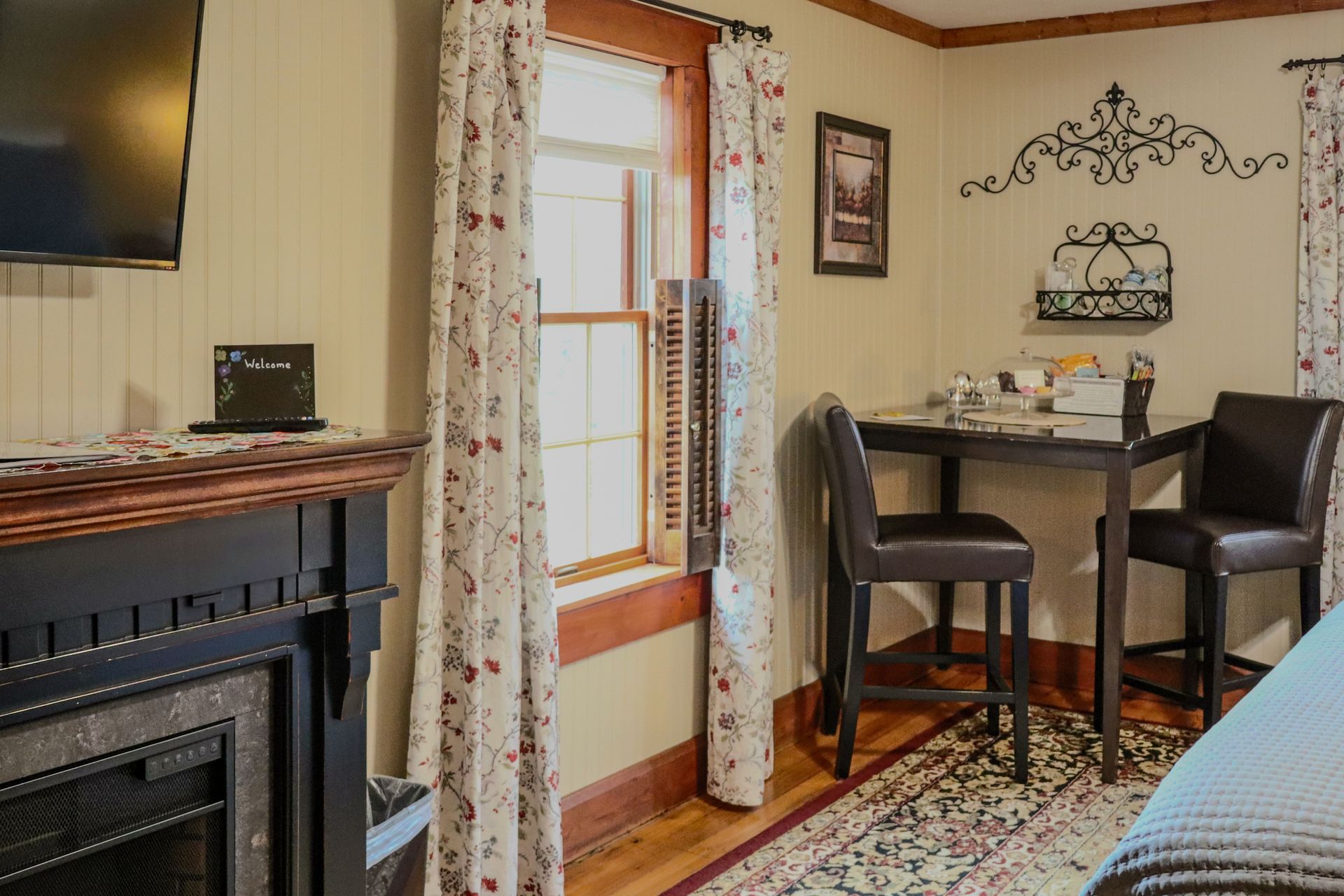 Cozy room with a fireplace, window, and a small table set for two. Soft lighting and floral curtains.