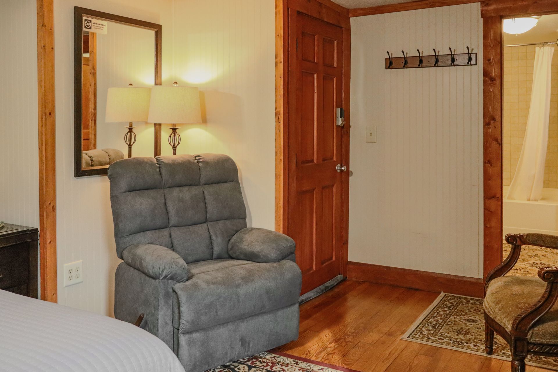 A cozy room with a recliner, vintage chair, wooden door, and a bathroom visible in the background.