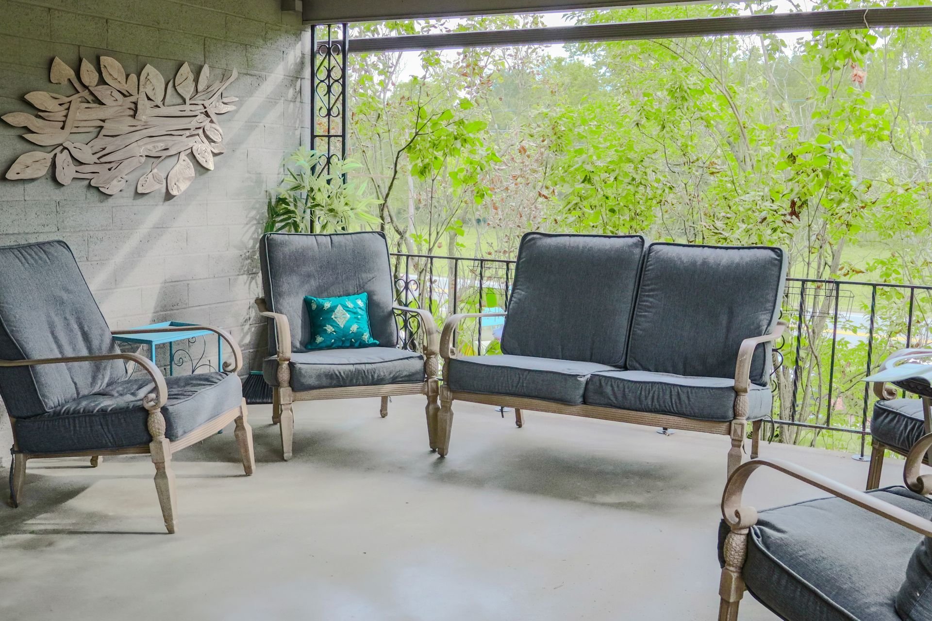 Outdoor seating area with gray cushions, a decorative wall piece, and a view of trees.