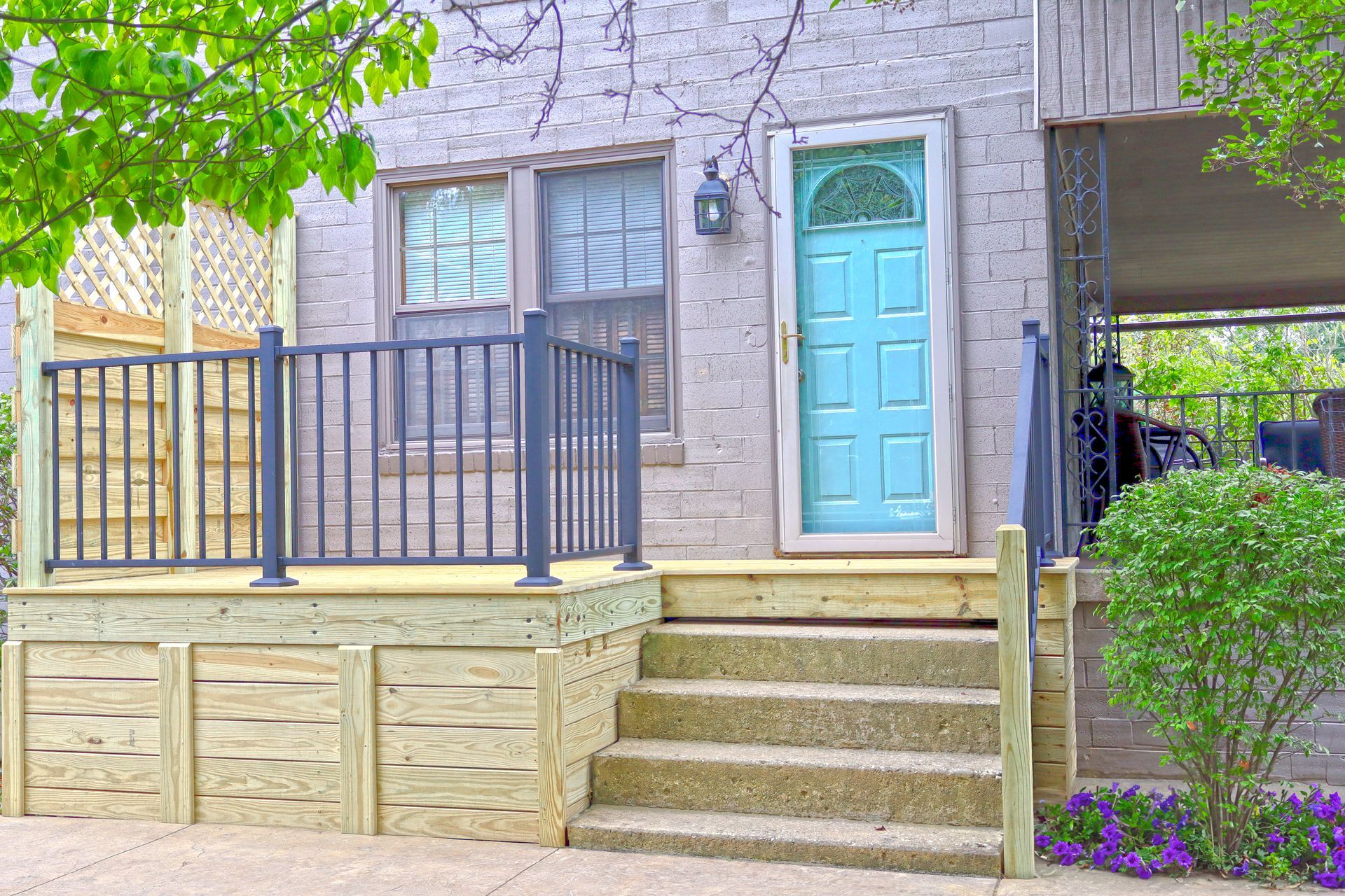 A light blue door with arched window, wooden steps, and a small porch with a black railing.