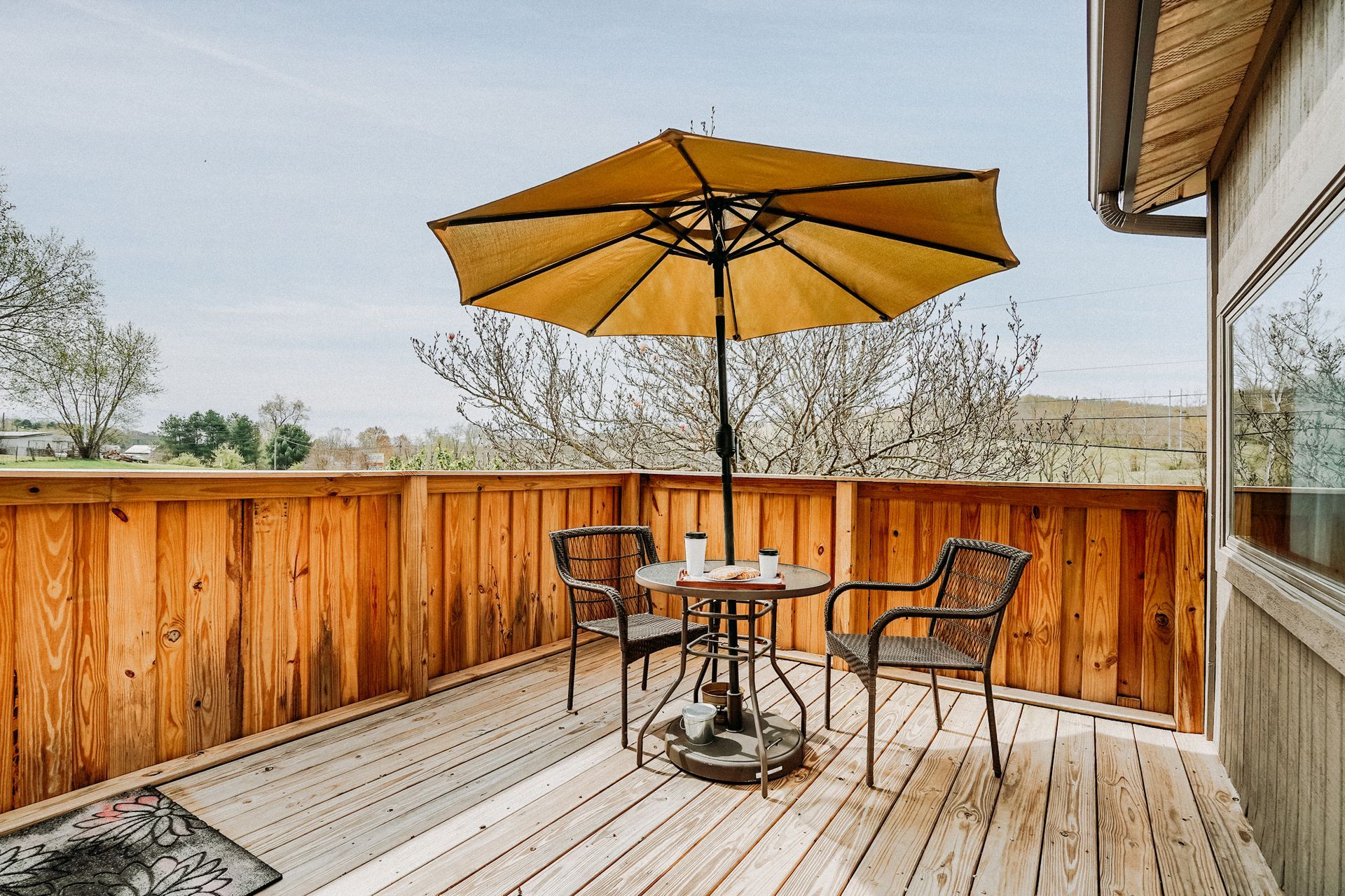 A small outdoor deck with a table, two chairs, and a yellow umbrella, overlooking a landscape.