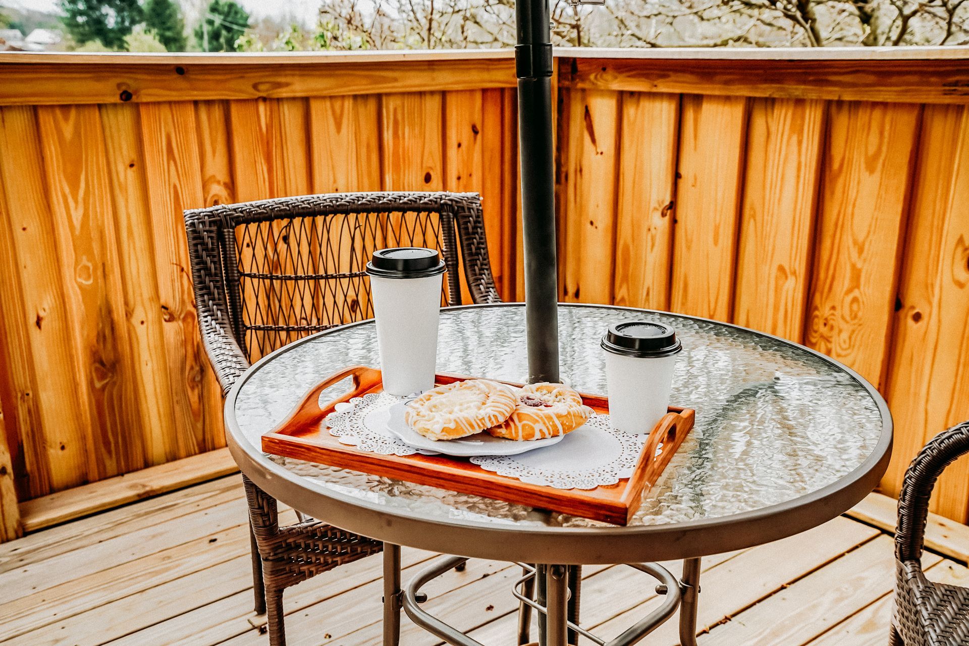 A sunny outdoor patio scene with a glass-top table, two coffees, and a tray with toast.