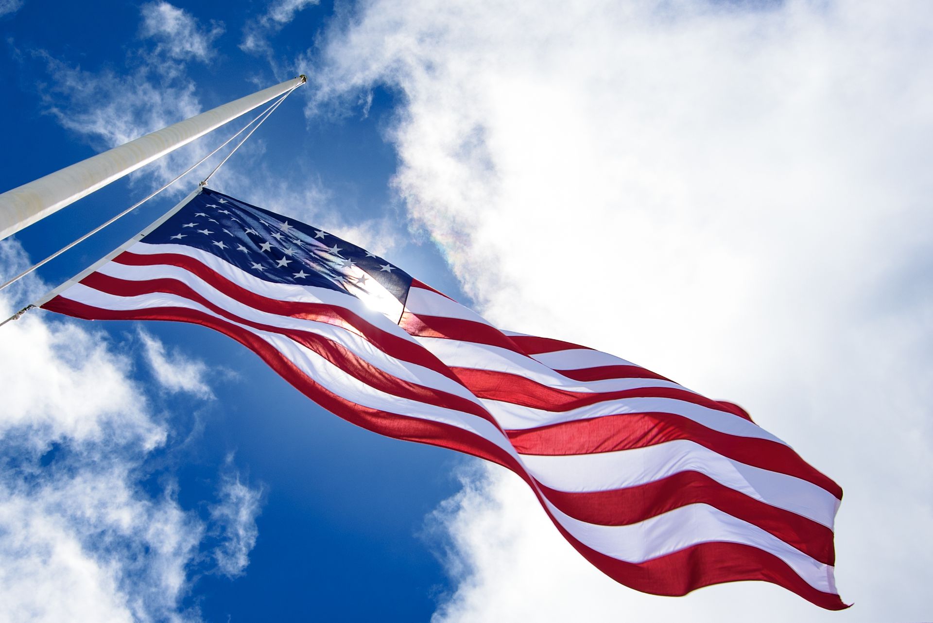 American flag waving against a bright blue sky with clouds