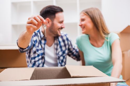 A man and a woman are sitting in a cardboard box holding keys to their new home.