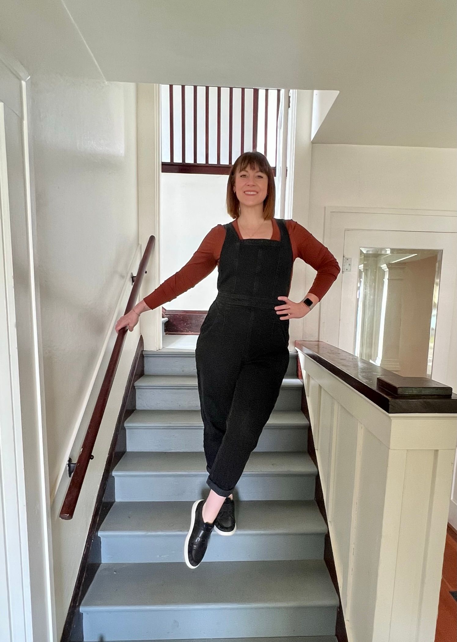 A woman in black overalls is standing on a set of stairs.