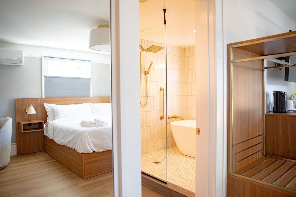 A bedroom with a bed , ottoman , lamps , and two windows.