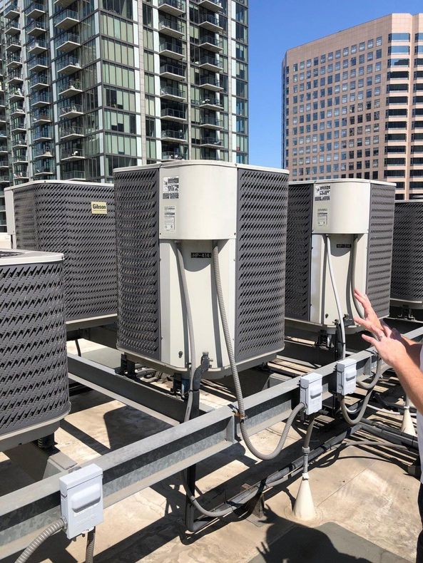 A person is standing on top of a roof with a bunch of air conditioners.