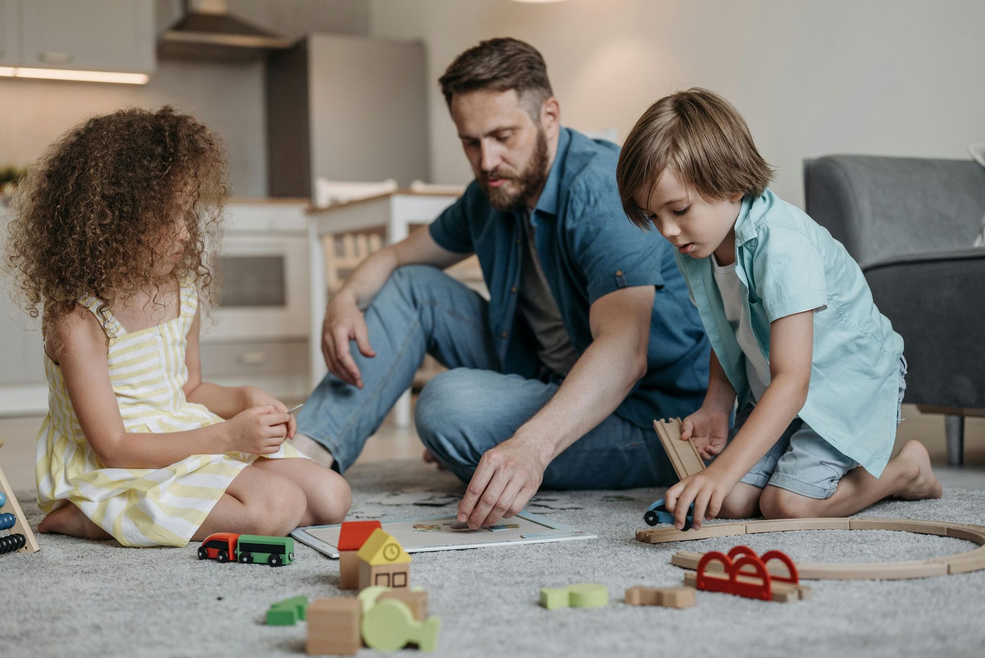 A man and two children are sitting on the floor playing with toys.