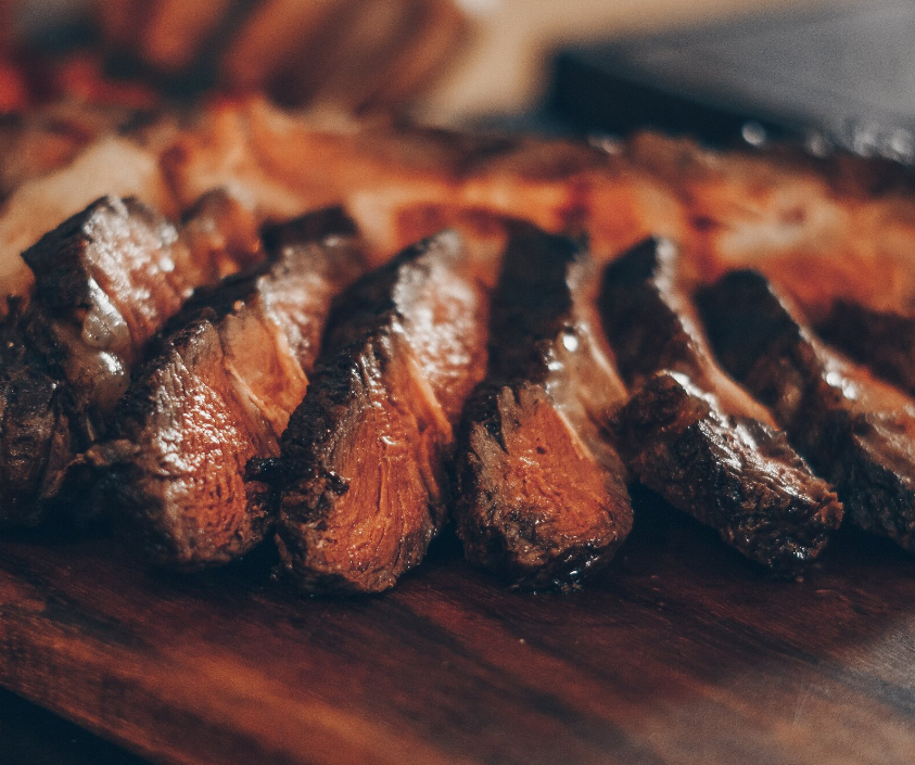 A close up of sliced steak on a wooden cutting board.