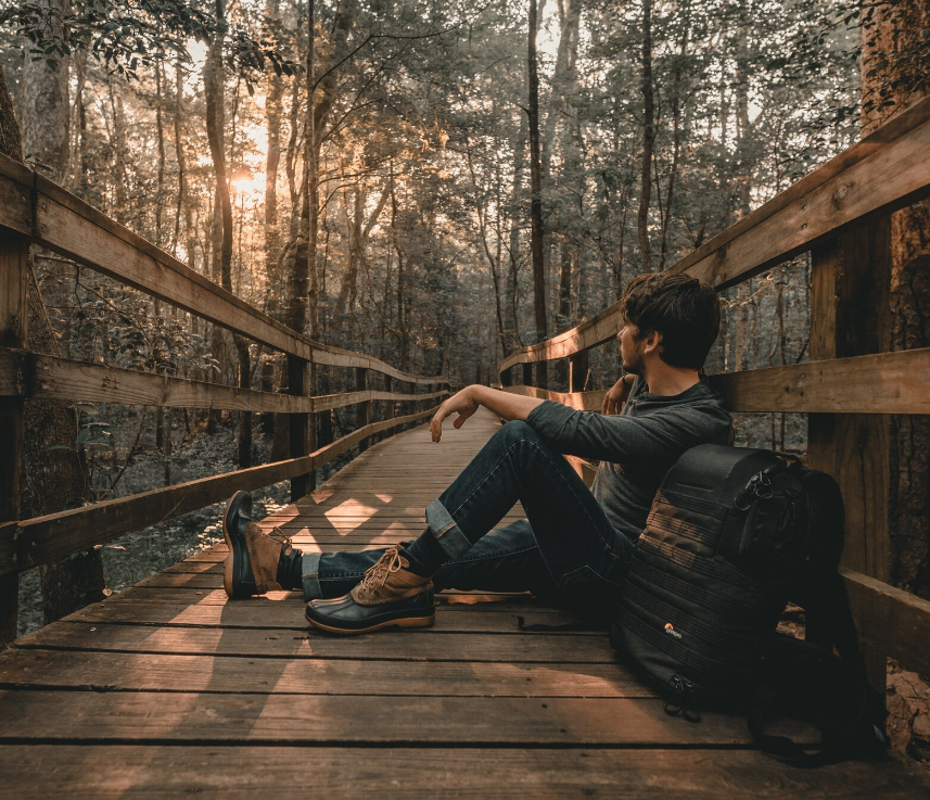 A man is sitting on a wooden bridge in the woods.