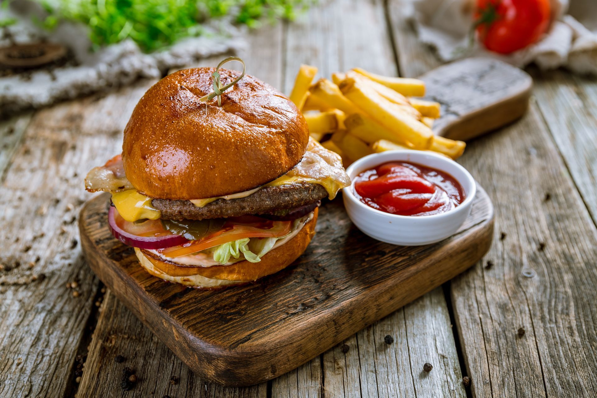 Cheeseburger with fries and ketchup on a wooden board, set on a weathered wooden table.