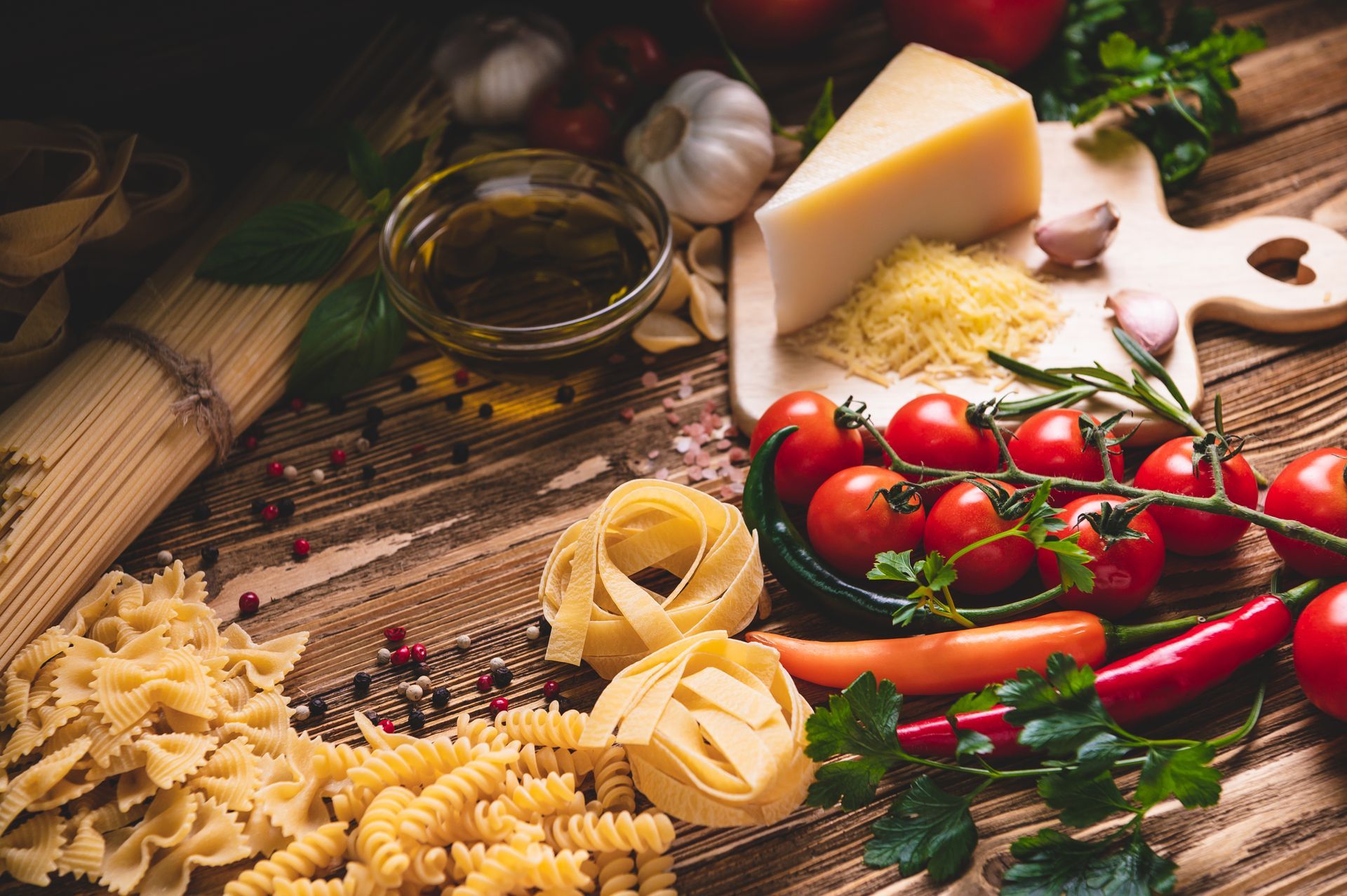 Pasta ingredients: tomatoes, garlic, cheese, pasta, pesto, and herbs on a wooden surface.