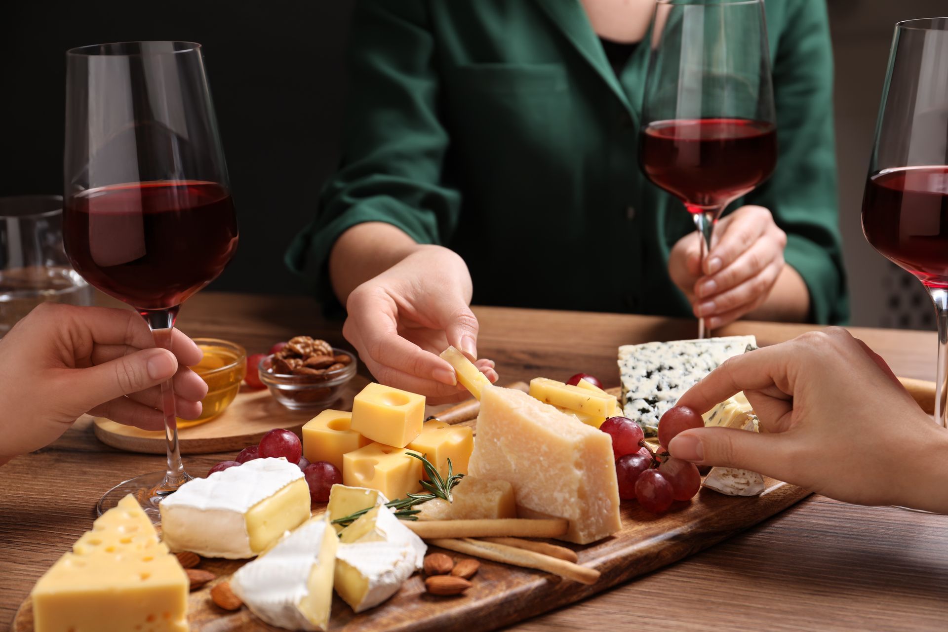 People enjoying cheese and wine with red wine glasses and cheese board.