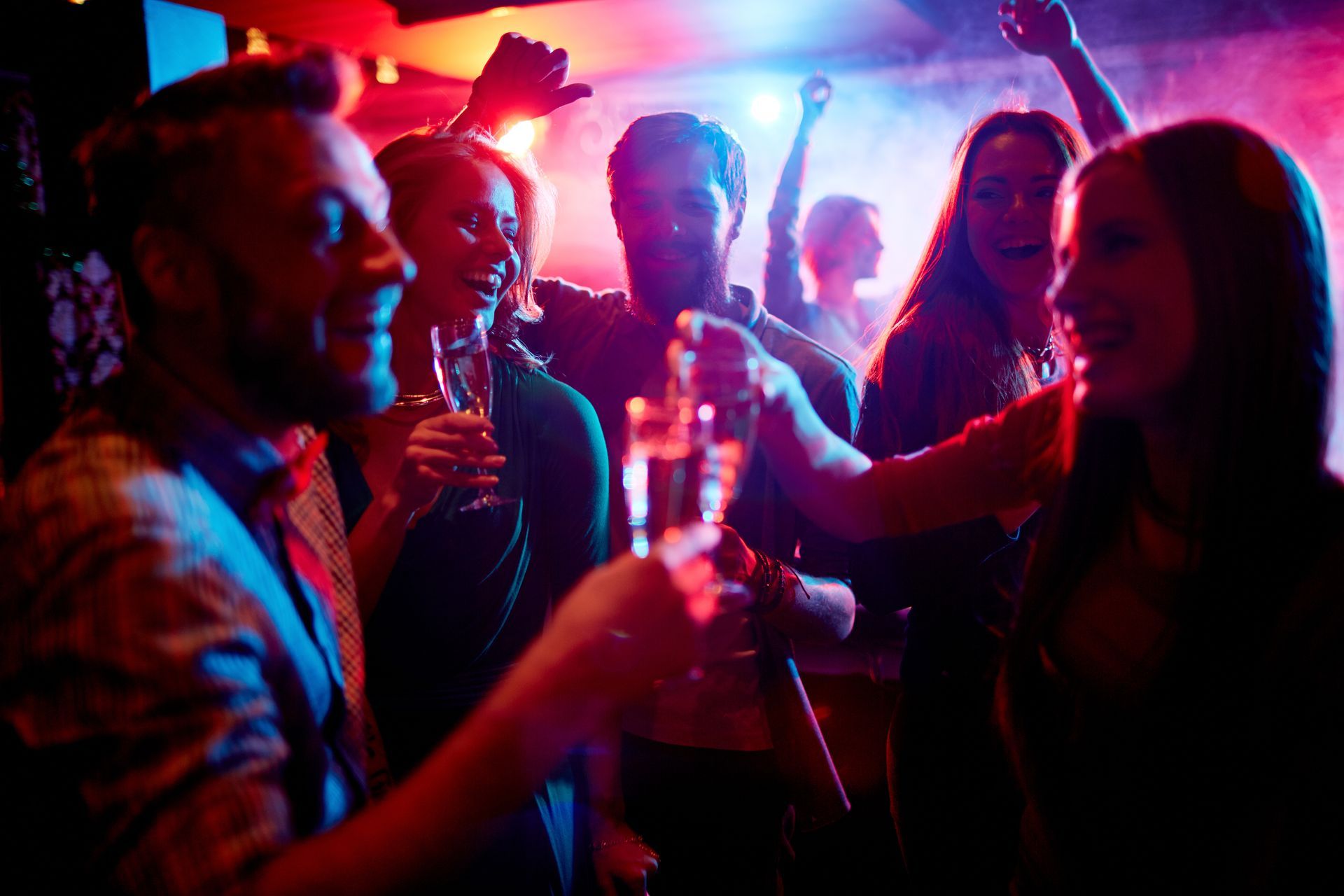 Group of people at a tailgate party, arms raised in celebration; food and drinks on the table.