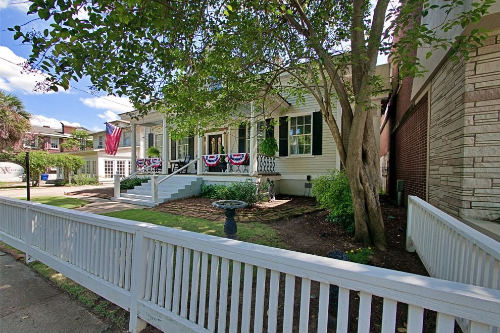 A white fence surrounds a large white house with a porch.