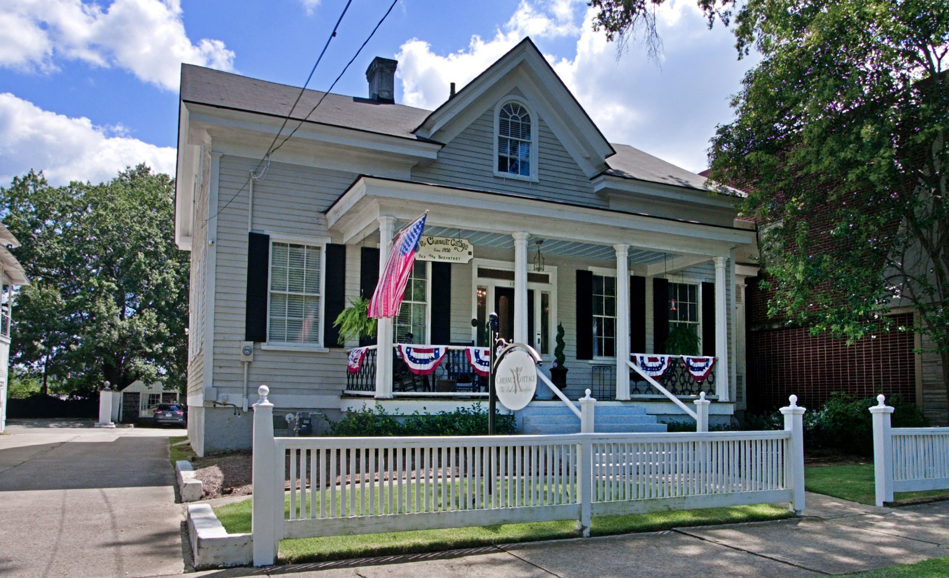 Light blue house with porch and white picket fence, American flag, and sign.