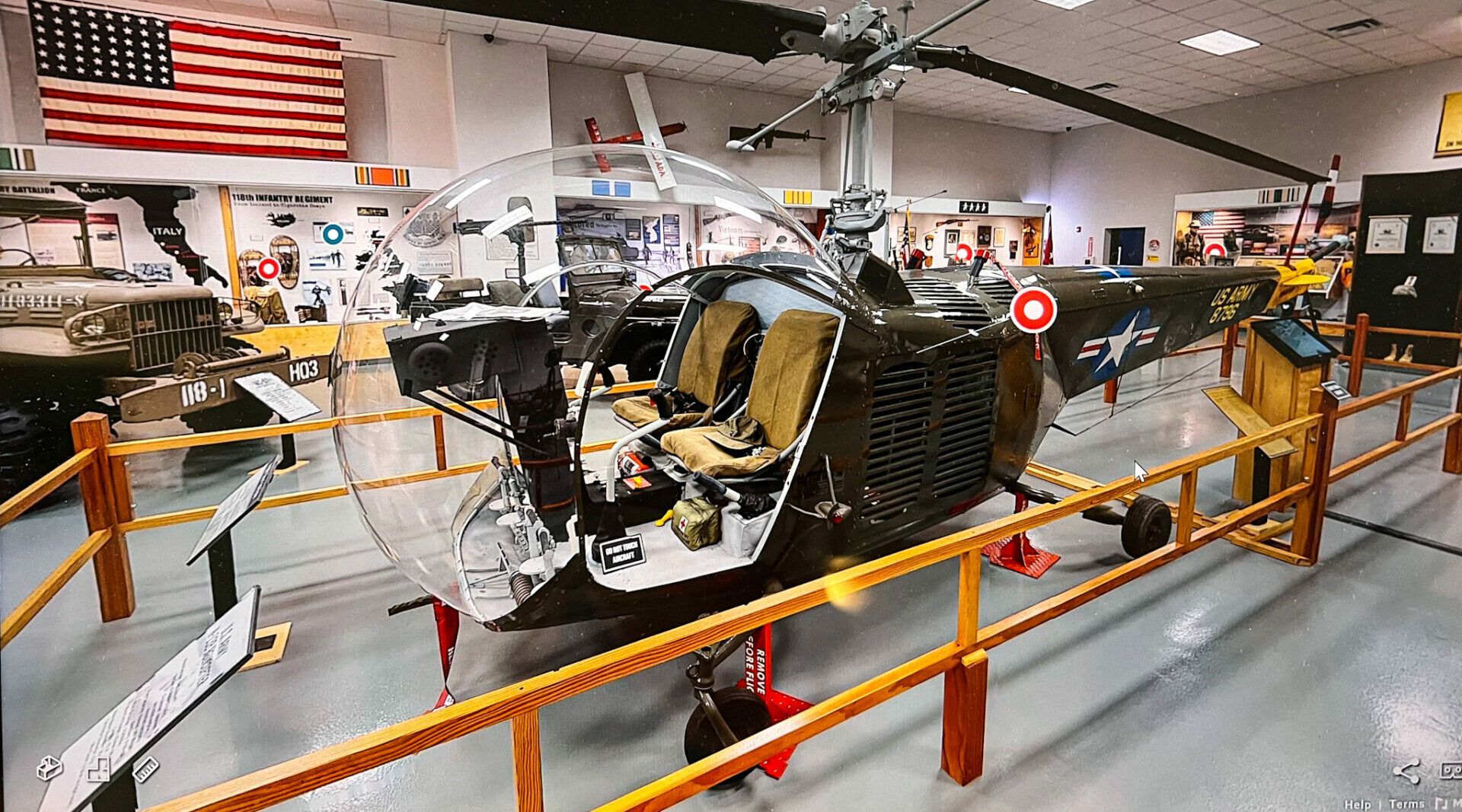 Helicopter on display at a museum, with an open cockpit, black exterior, and an American flag in the background.