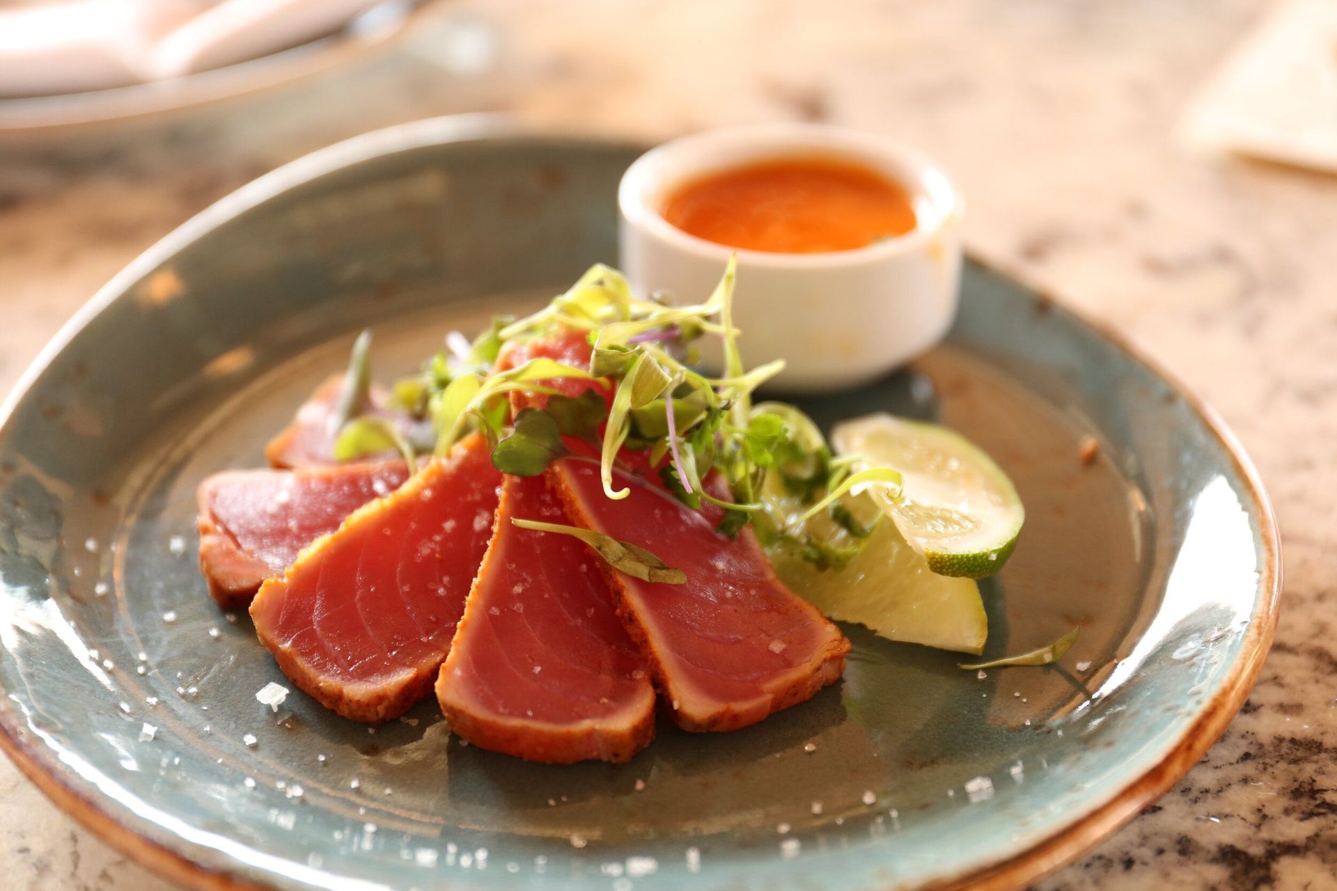 Seared tuna slices with greens, lime, and sauce on a blue plate.