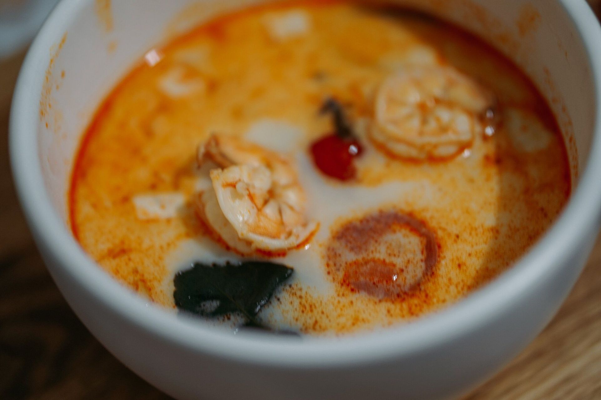 Close-up of a white bowl filled with orange Tom Yum soup, shrimp, and creamy coconut milk.