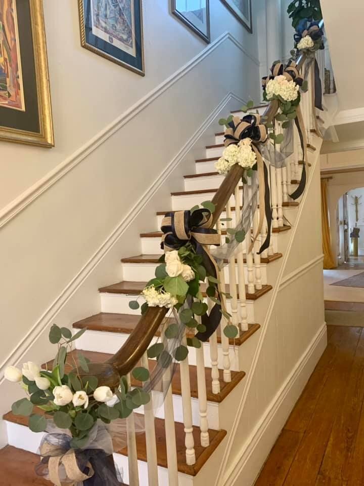 Staircase decorated with white flowers, greenery, and black and silver ribbons.