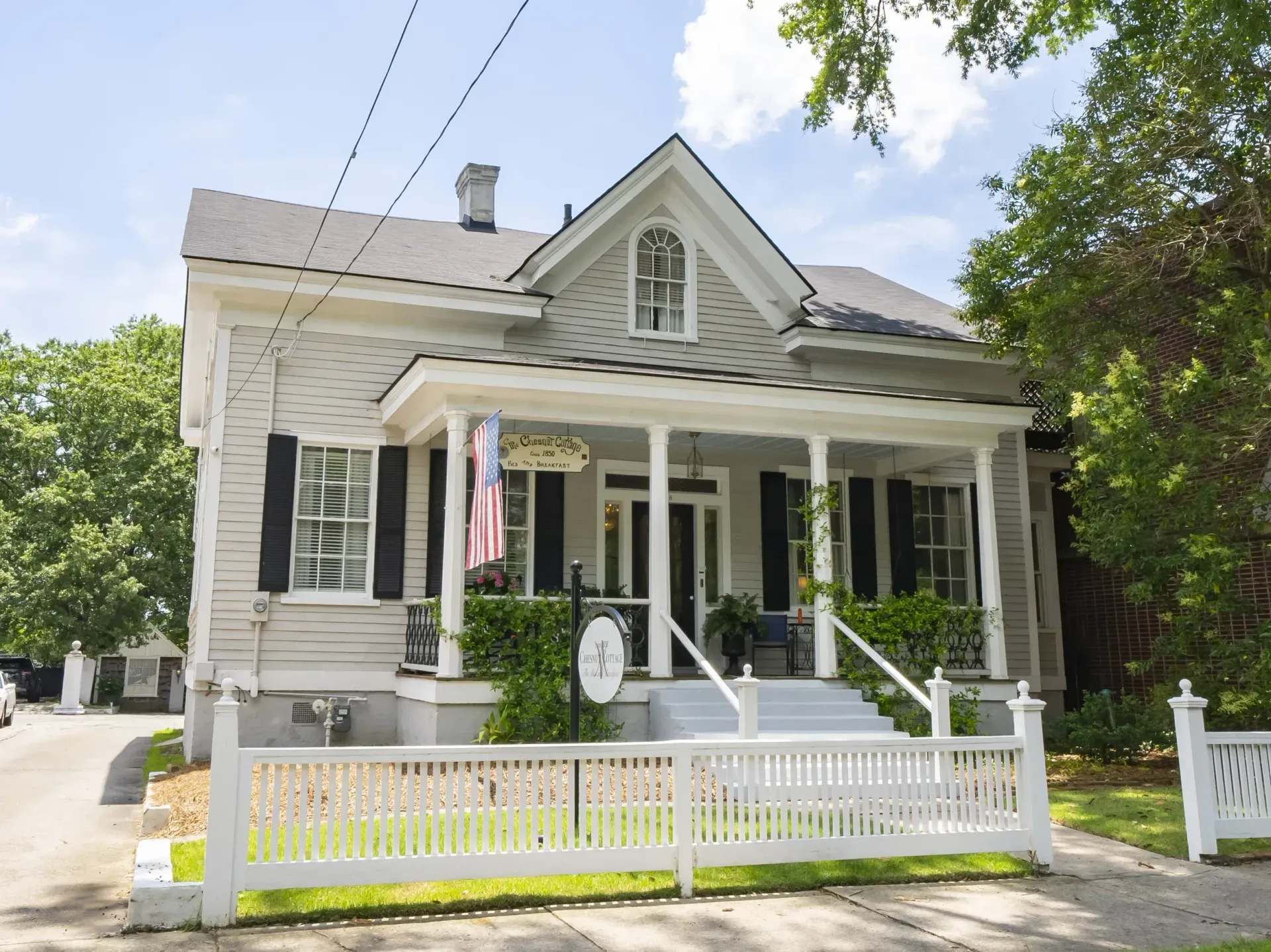 Gray Victorian house with white porch, picket fence, and American flag.