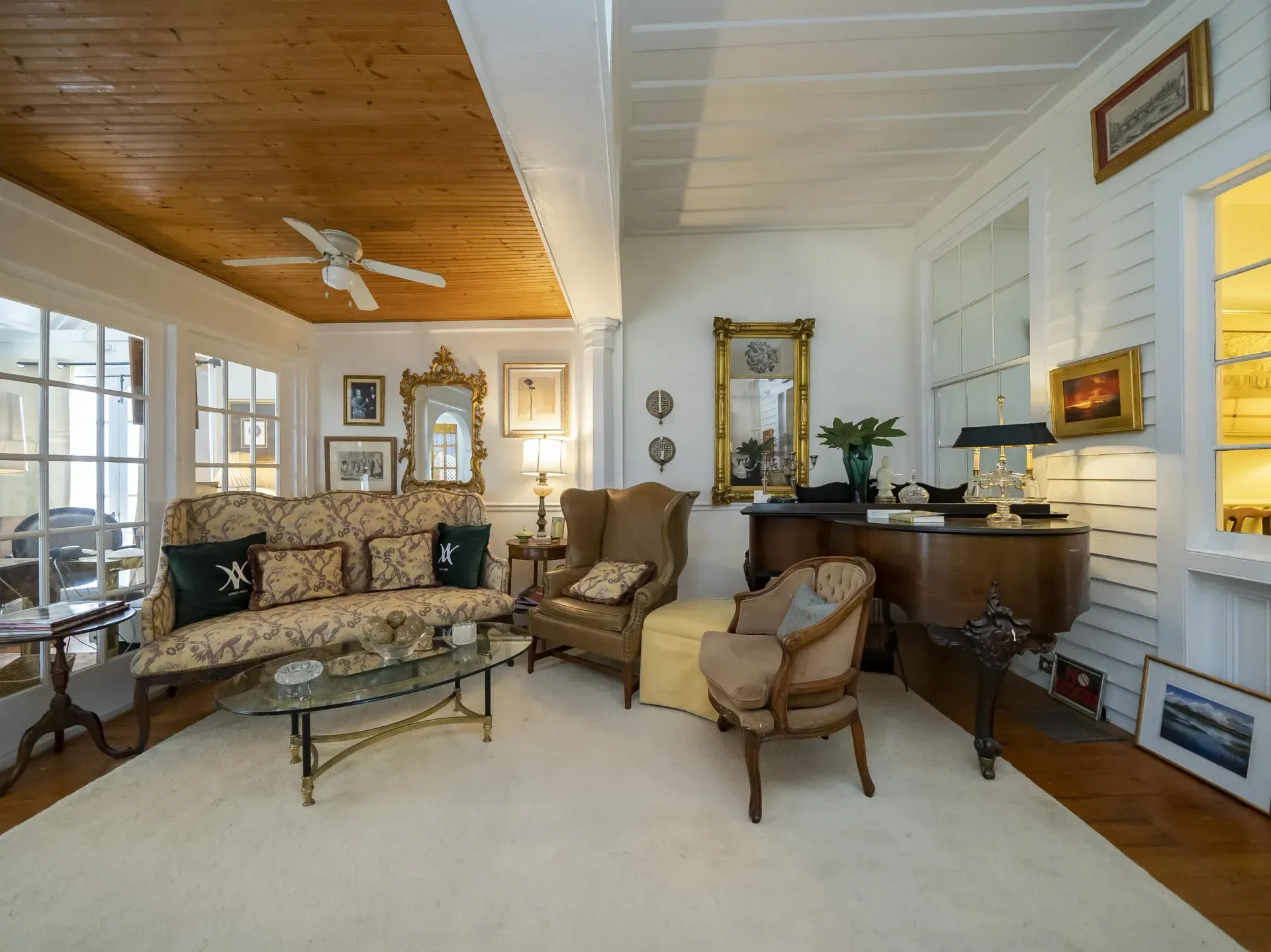 Living room with patterned sofa, armchairs, gold mirrors, and wood ceiling.