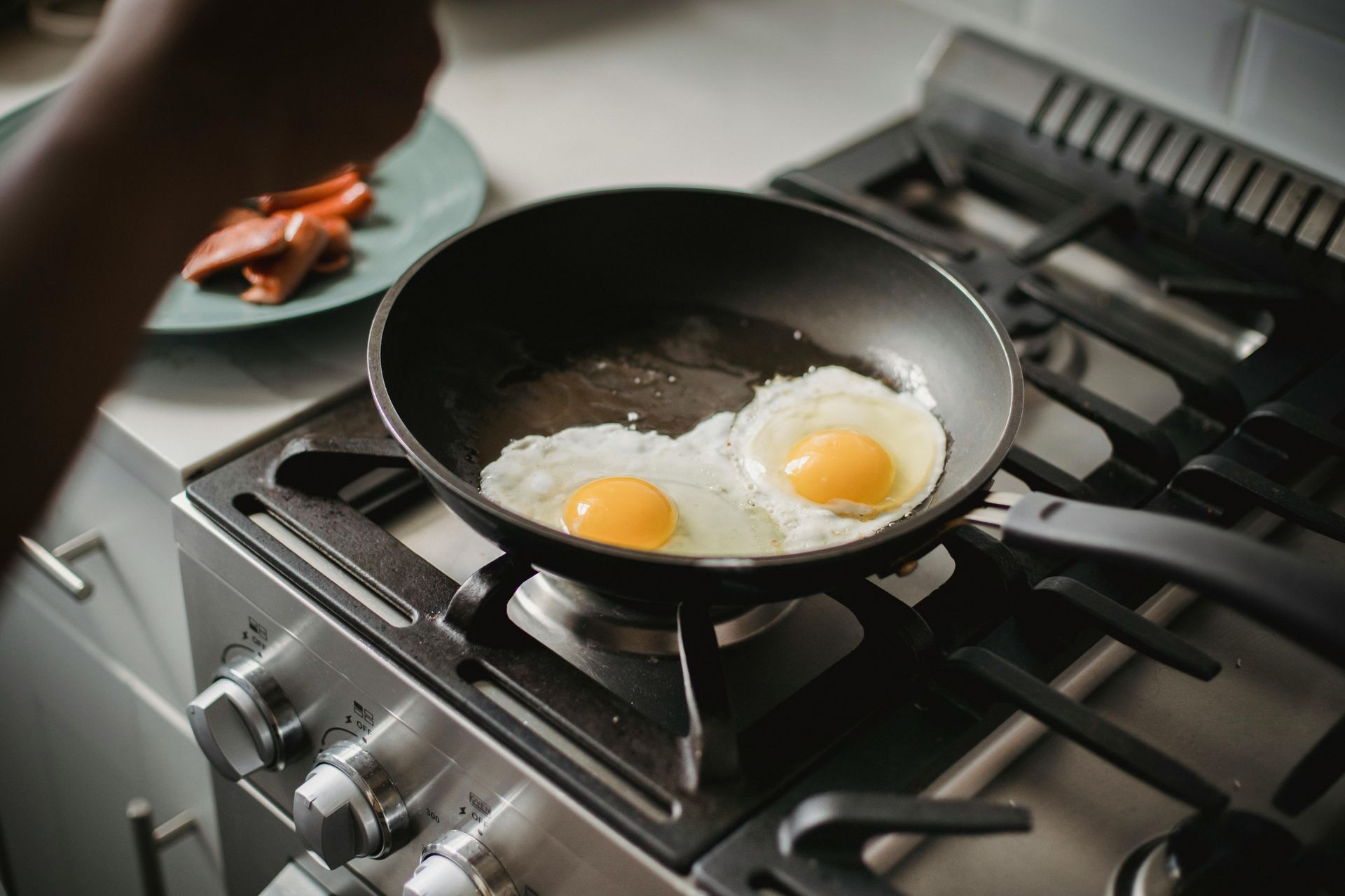 A person is cooking eggs in a frying pan on a stove.