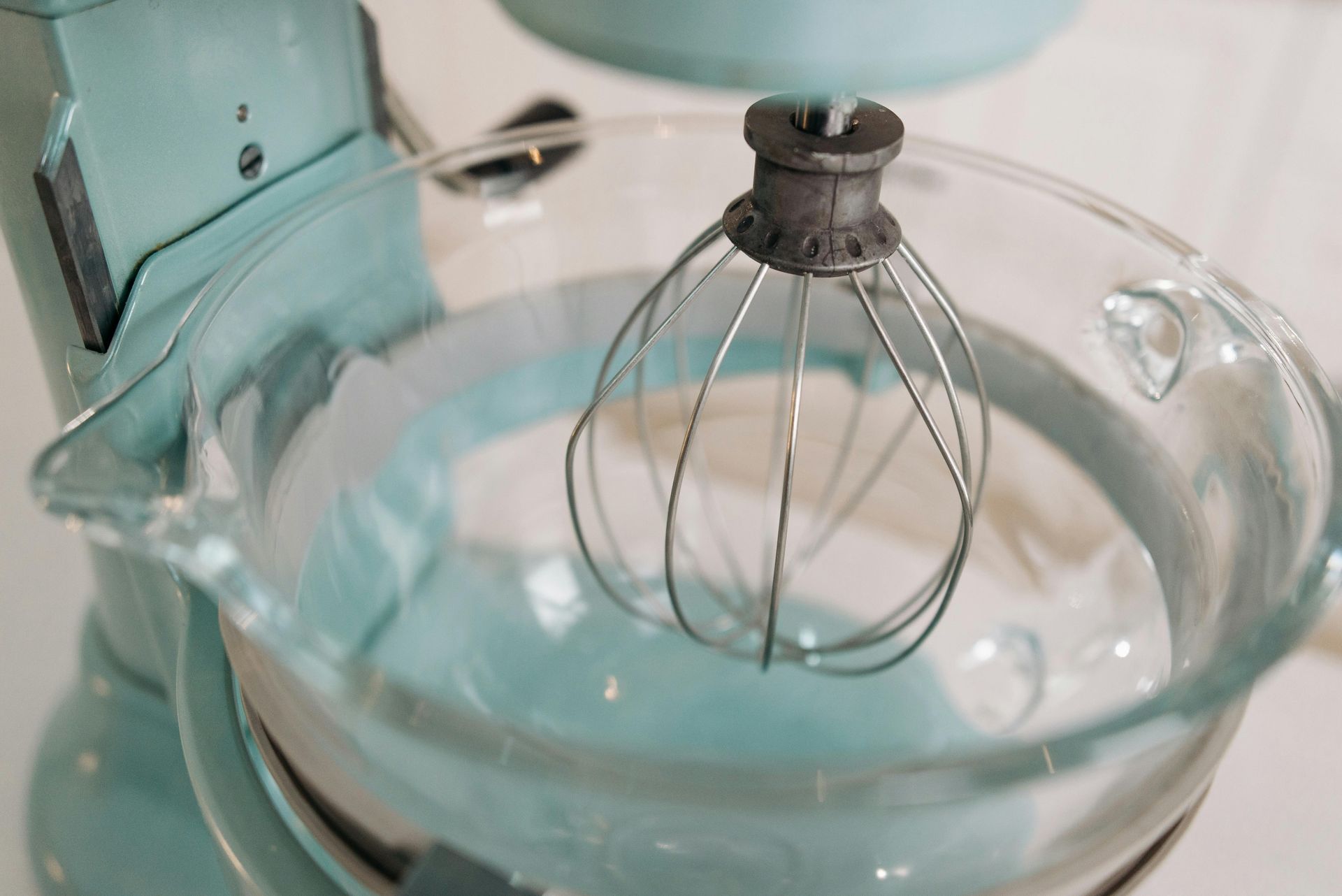 A close up of a mixer with a whisk in a glass bowl.